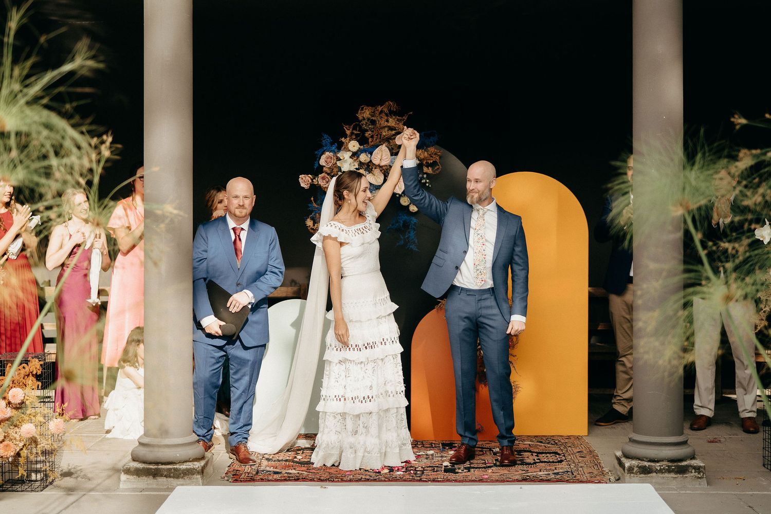 A joyous celebration unfolds on a columned porch decorated with bright florals and a yellow arch.