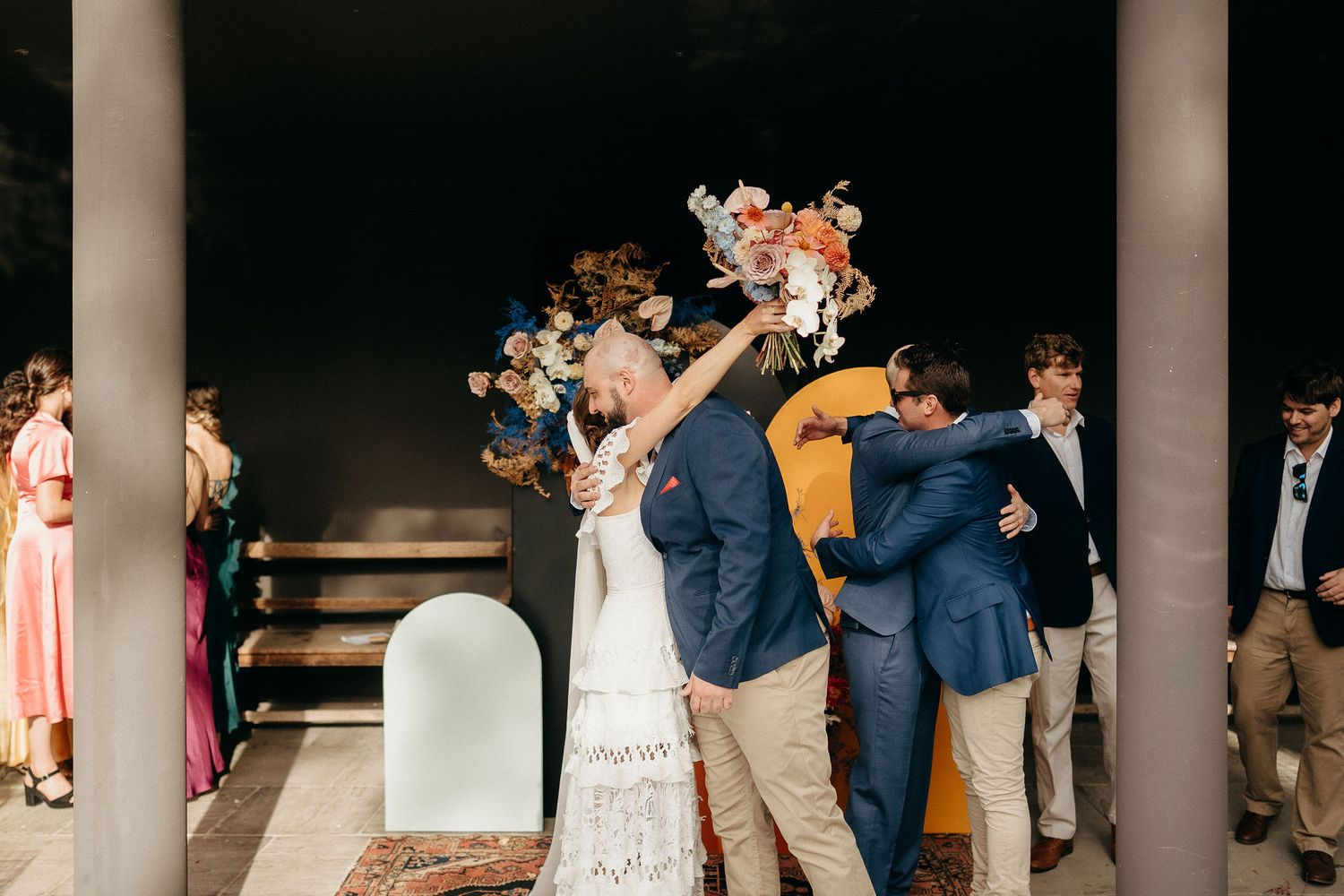 Wedding couple celebrates by joyfully breaking a cake or dessert item together during outdoor reception.