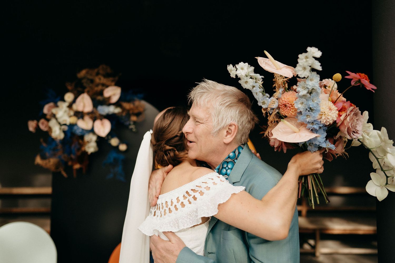 Two people embrace during a romantic wedding moment with a beautiful floral bouquet and decorative backdrop.