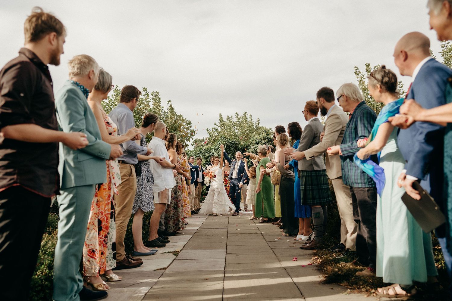 Wedding guests line a walkway as a couple makes their way down the path during an outdoor ceremony.