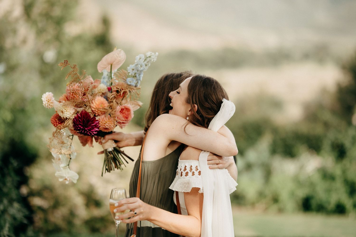 A romantic outdoor embrace with a stunning floral bouquet featuring peach and red blooms against a natural landscape.