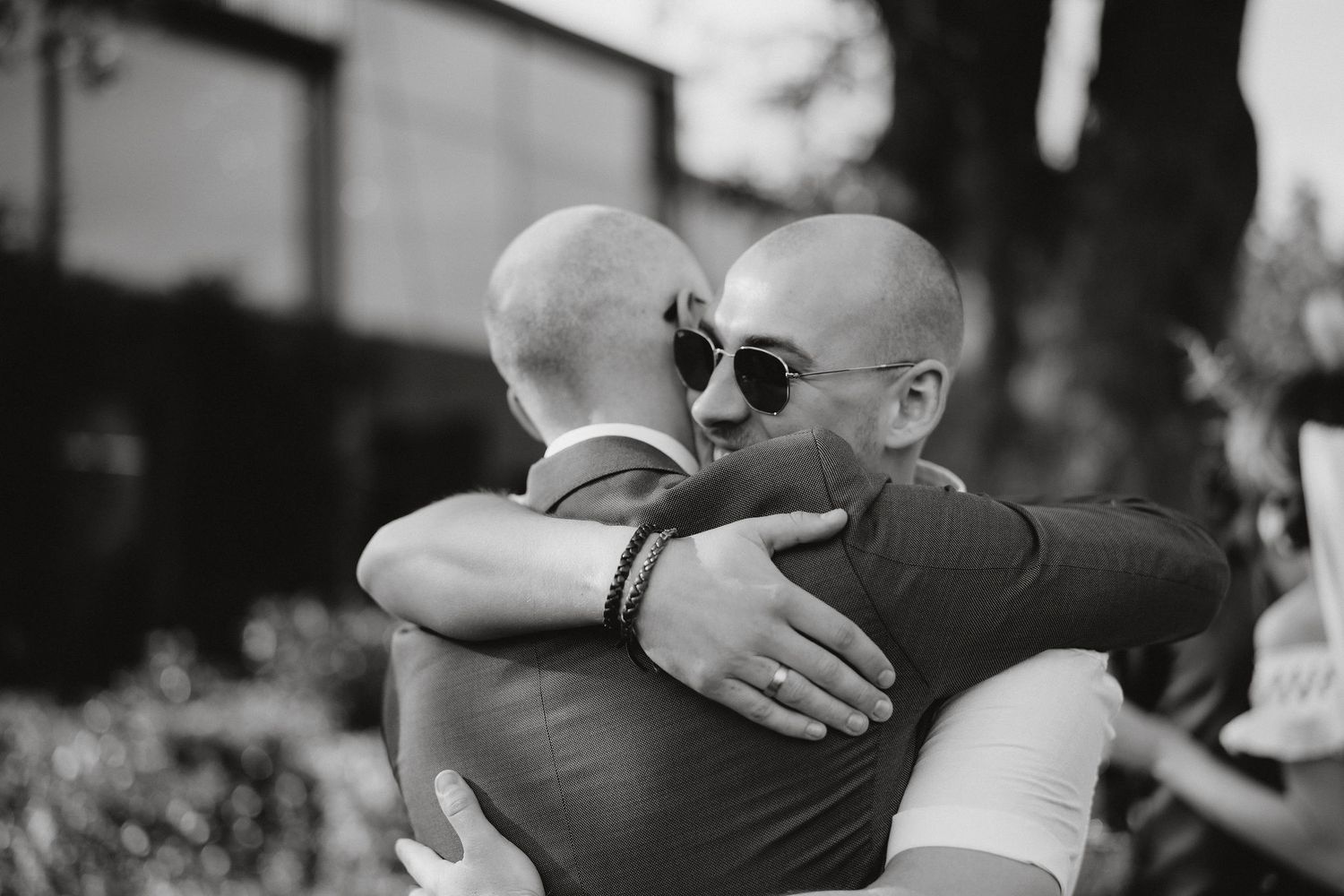 Two people wearing sunglasses share an emotional embrace outdoors in black and white photography.