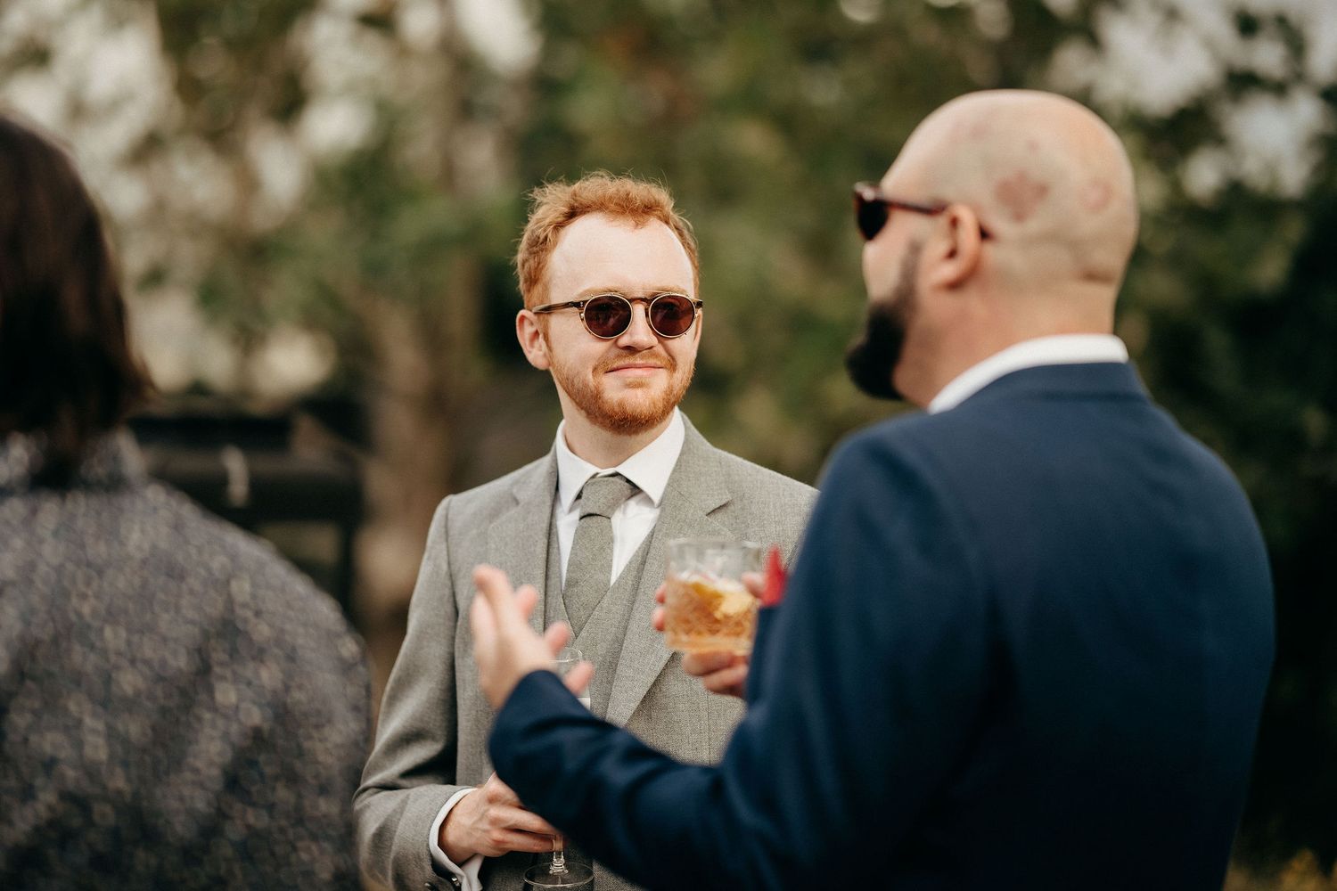 Two people engaged in conversation during an outdoor wedding celebration with natural foliage in the background.