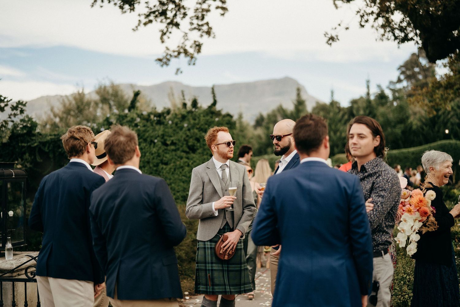 A group gathers outdoors at an elegant reception with mountain views and natural scenery in the background.