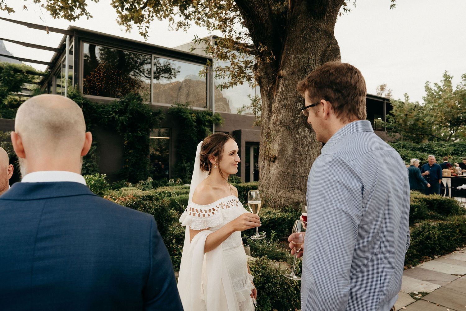 People chatting together at an outdoor wedding event in a garden setting with warm afternoon light.