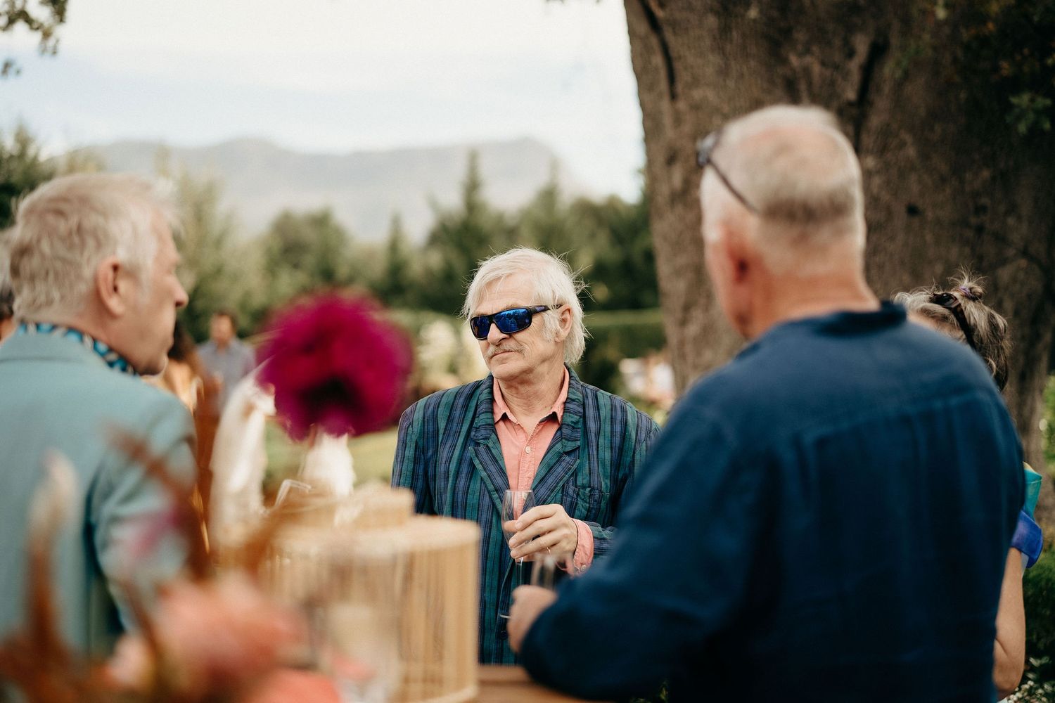 People gathered outdoors for social conversation on a sunny day with mountains visible in the background.
