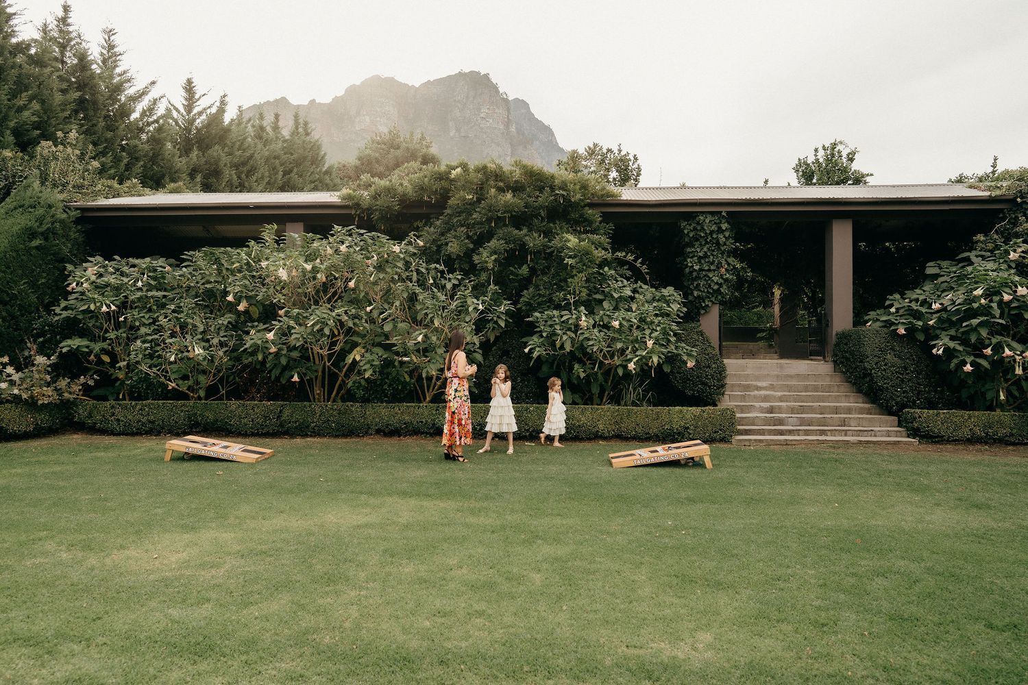 Three people stand on a manicured lawn in front of a mid-century modern house with mountain views in Hawaii.