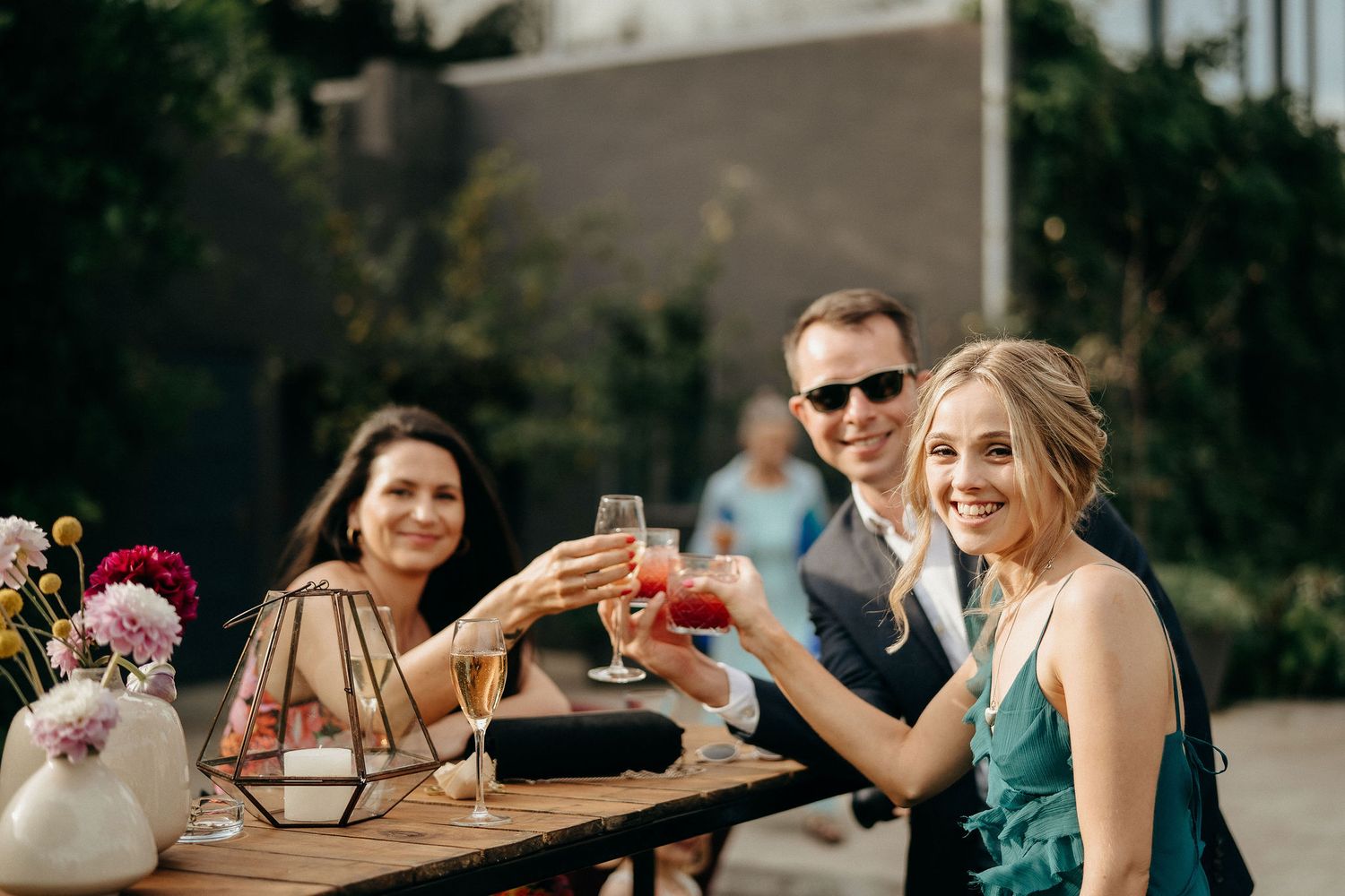 Friends toasting with colorful cocktails while sitting at an outdoor table on a sunny afternoon.