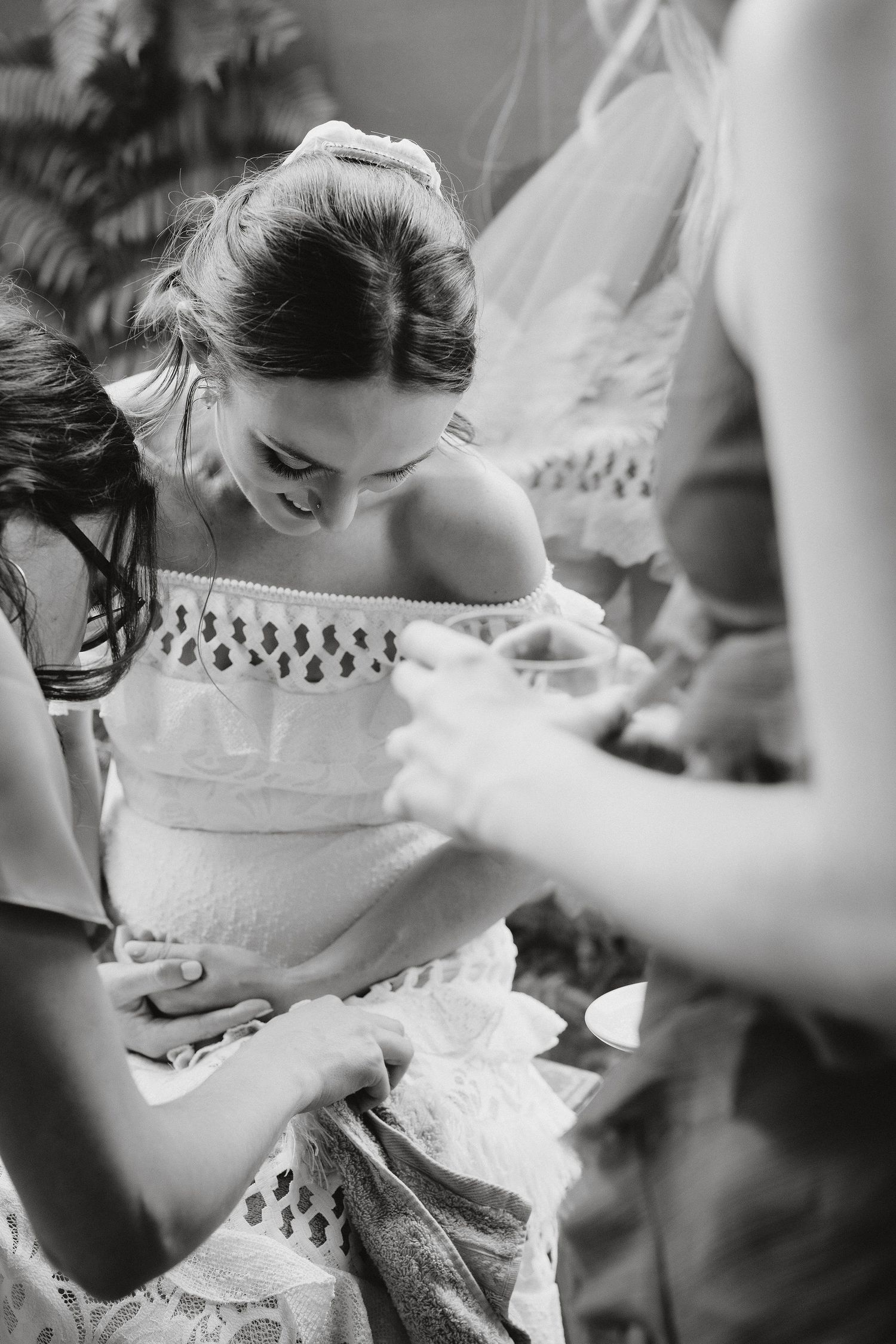 Black and white photo of woman in white dress looking down at wedding dress details being prepared with vintage style.