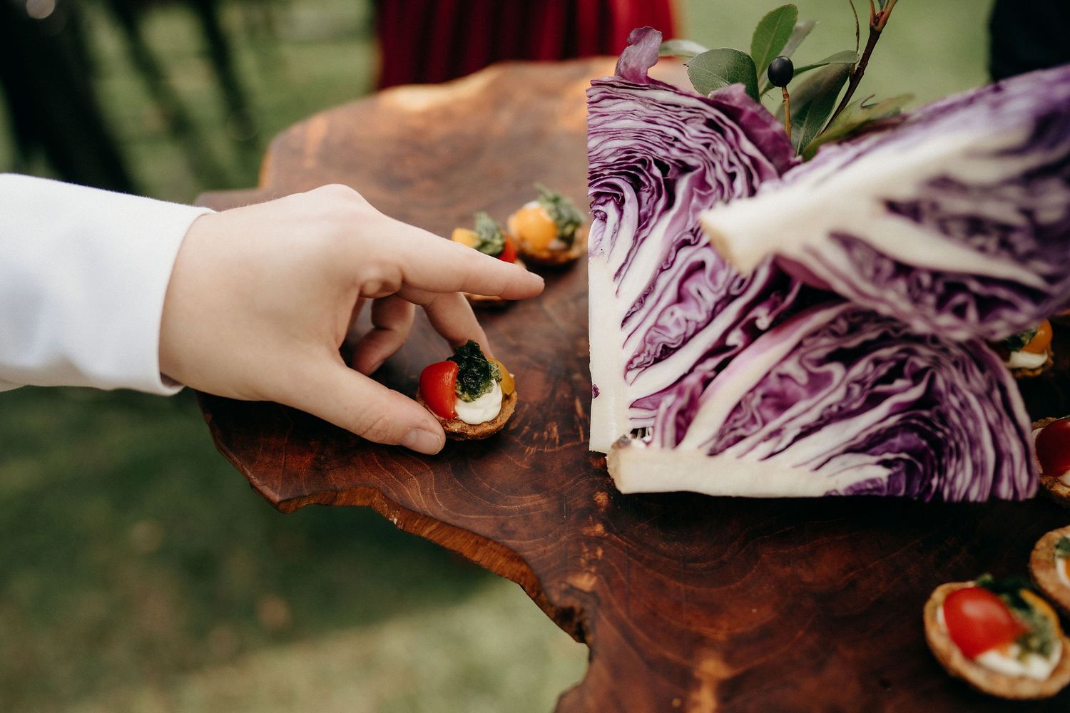 Hand reaching for fresh vegetables on wooden cutting board next to vibrant purple cabbage.