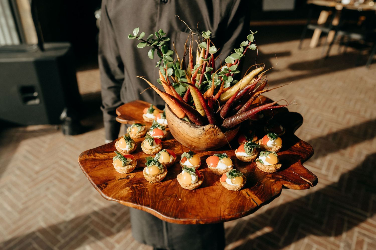 Elegant catering platter featuring small appetizer bites and decorative floral garnishes on a rustic wooden serving board.