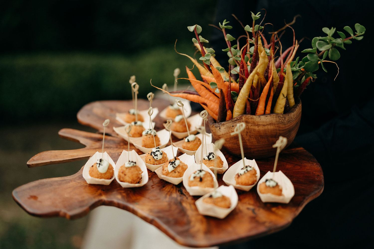 Appetizers on a wooden serving board with fresh carrots and stuffed pastries arranged for catering service.