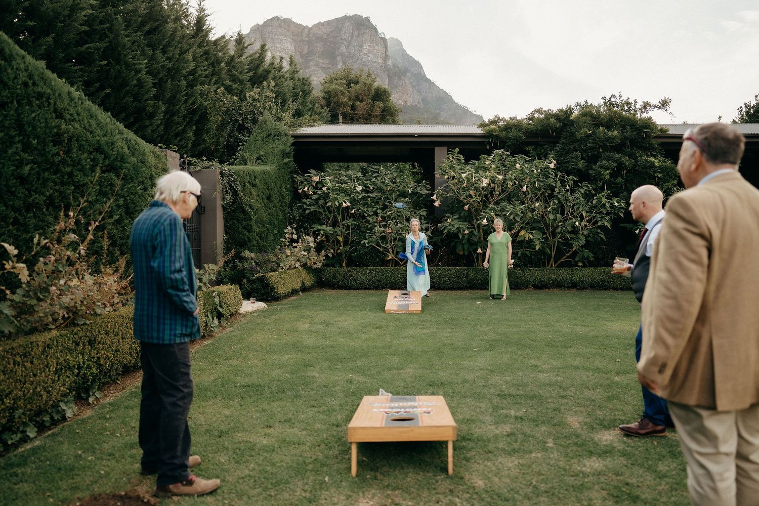 A garden lawn game setup with a wooden board beneath an arbor surrounded by mountains and lush greenery.
