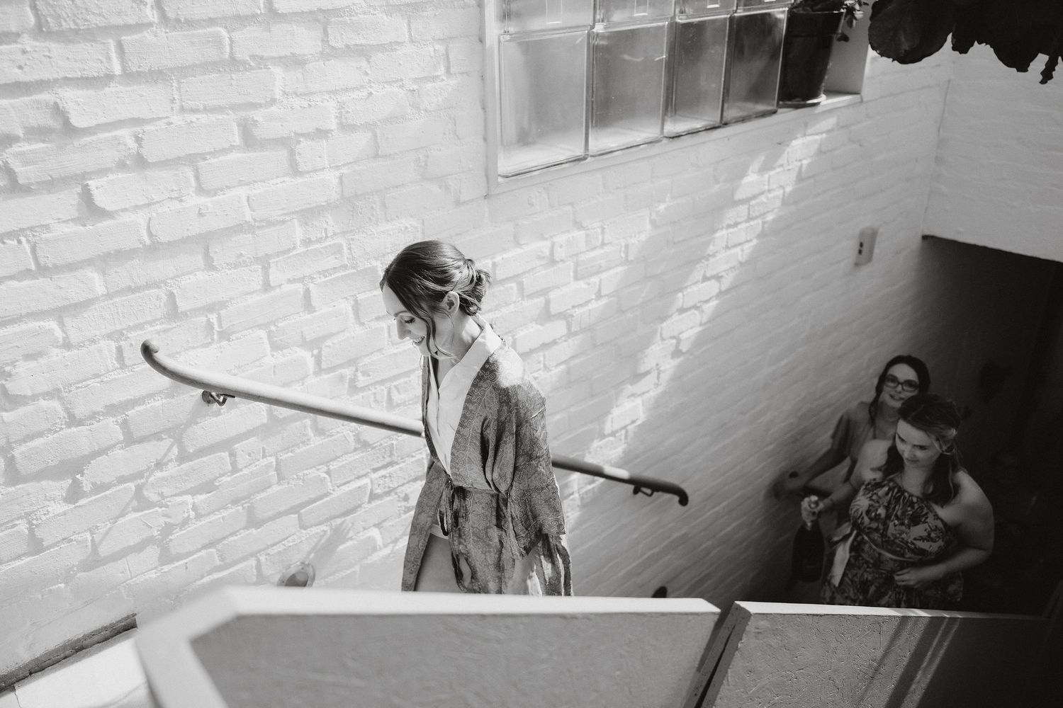 A person descends a staircase while holding onto a railing in front of a white brick wall.