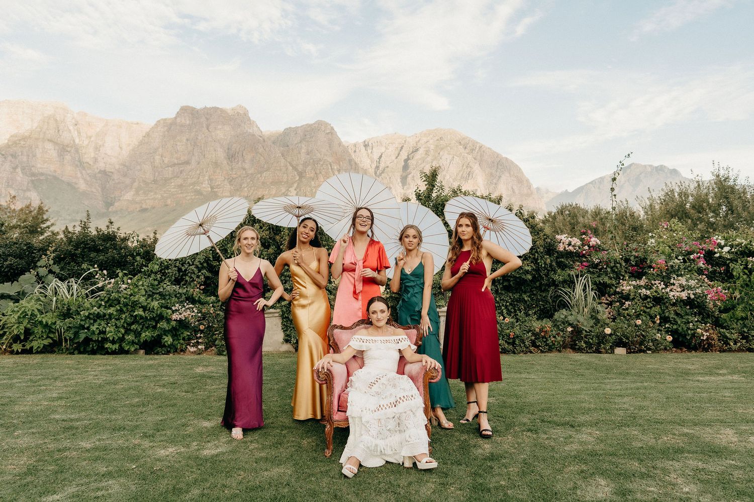 A bridal party poses together on a lawn with snow-capped mountains and greenery in the background.
