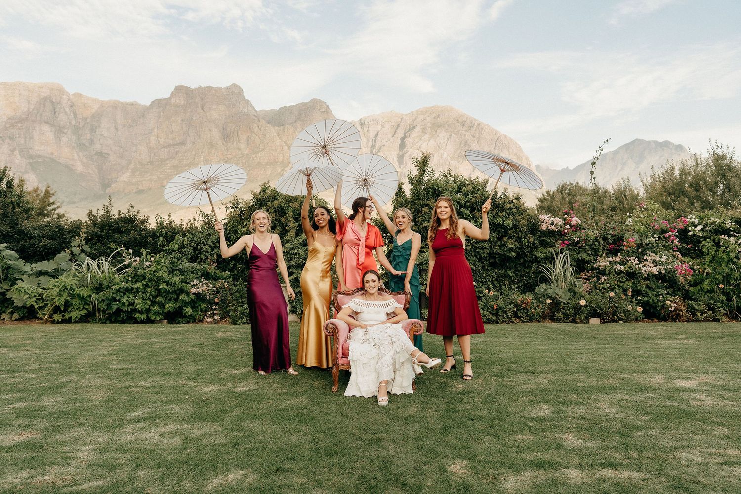 Wedding party poses on green lawn with majestic mountain backdrop at outdoor celebration.