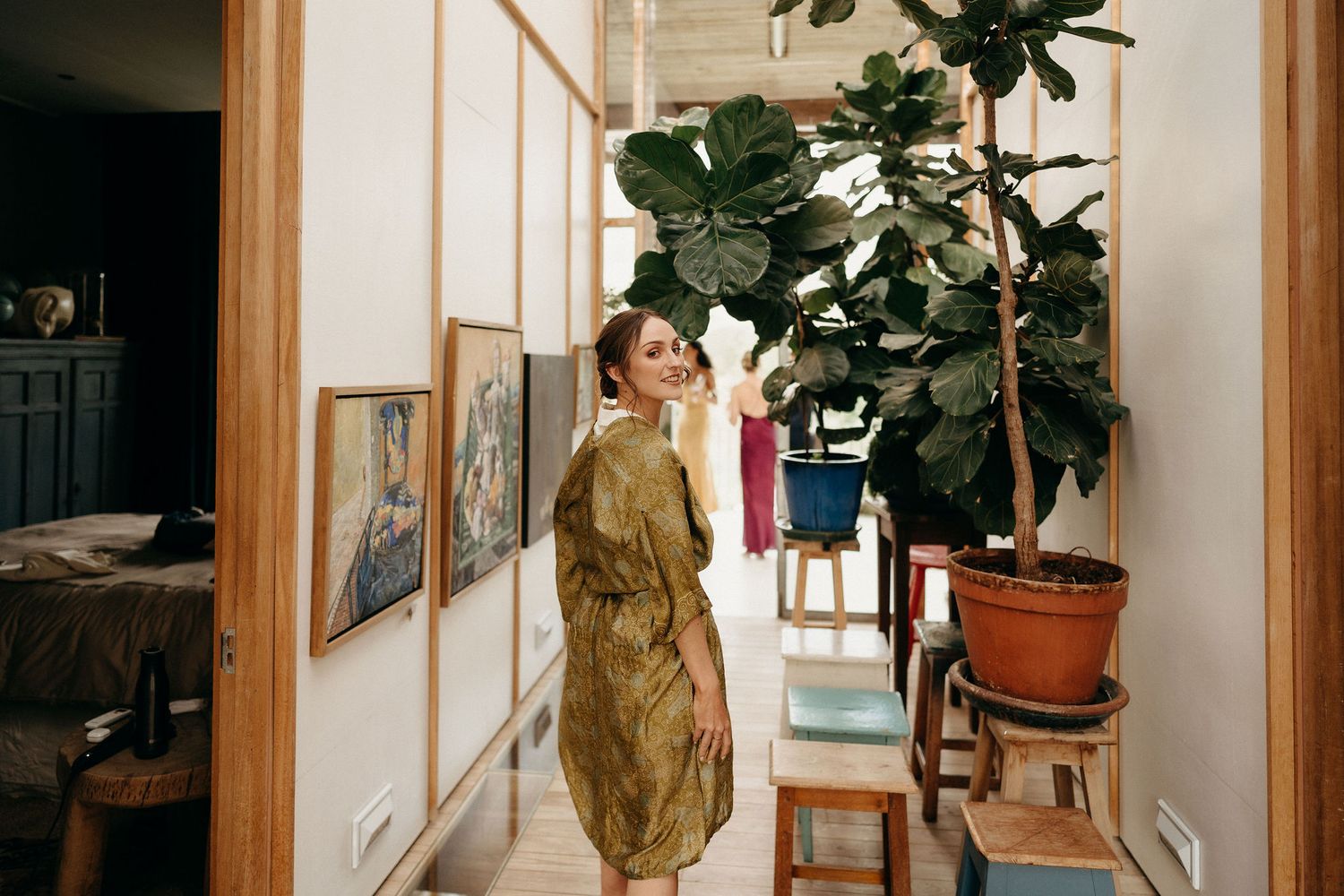 A corridor adorned with framed art and a large potted fiddle leaf fig plant creates an elegant indoor setting.