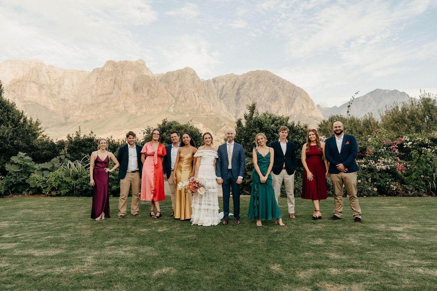 Wedding party stands on lawn with dramatic mountain peaks in background at outdoor desert venue.