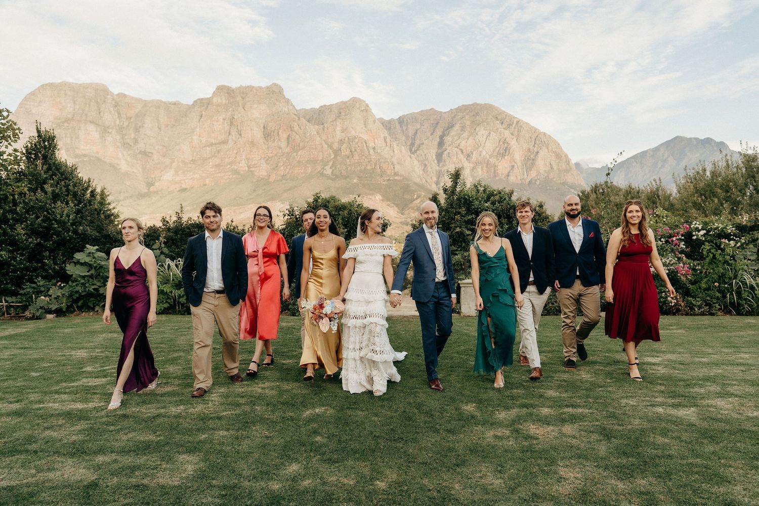 Wedding party walking together across a green lawn with majestic desert mountains in the background.