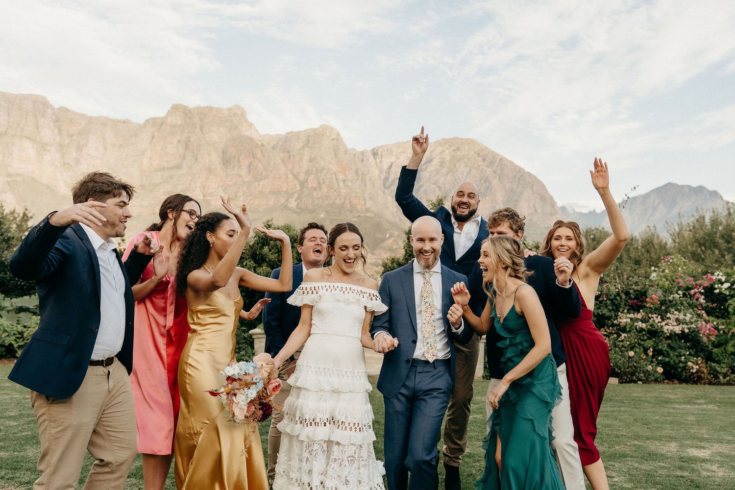 Joyful celebration at outdoor wedding with wedding party in colorful dresses against scenic mountain backdrop.