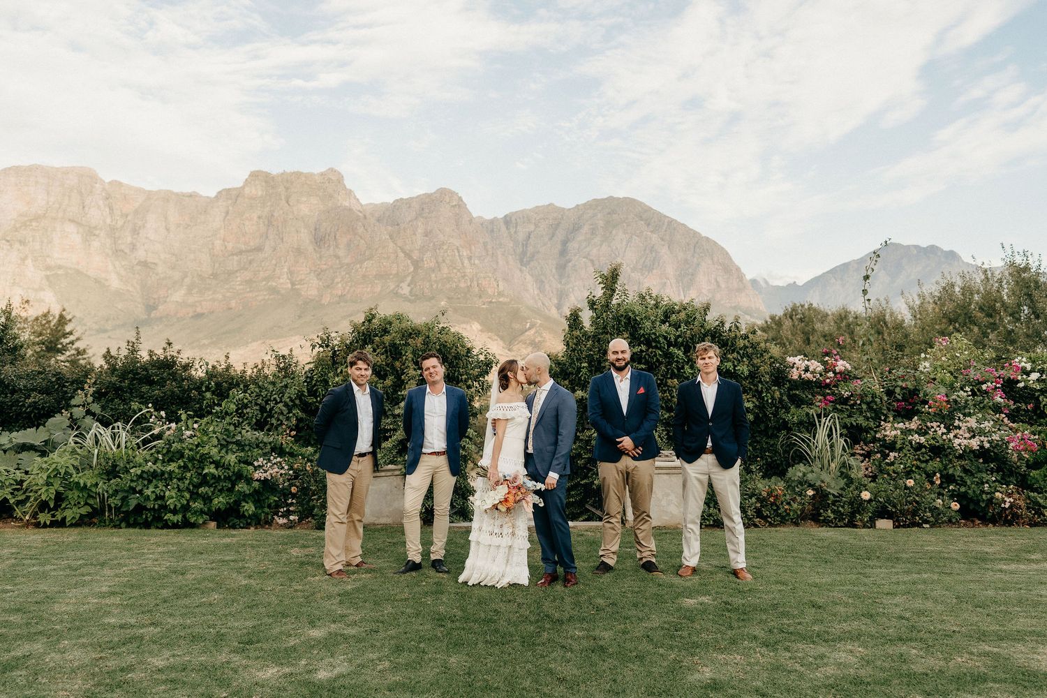Wedding party stands on manicured lawn with dramatic mountain backdrop in Cape Town.