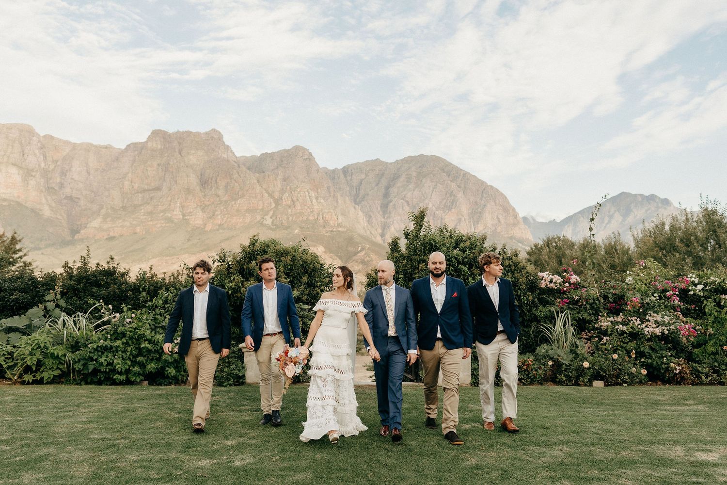 Wedding party poses on a manicured lawn with dramatic mountain backdrop and blooming garden in Cape Town.