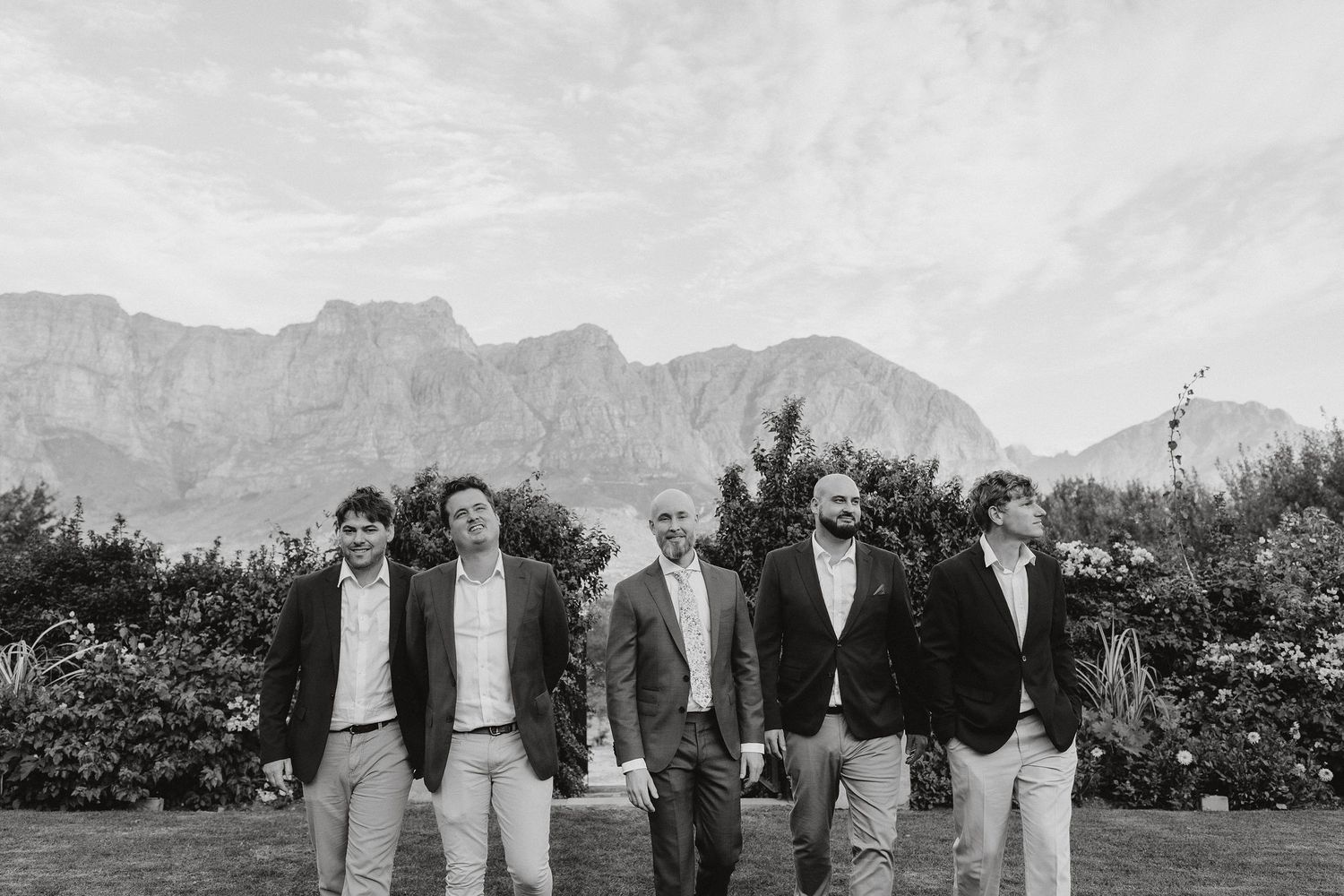 A group of people stand in formal attire against a backdrop of dramatic mountain peaks in black and white.