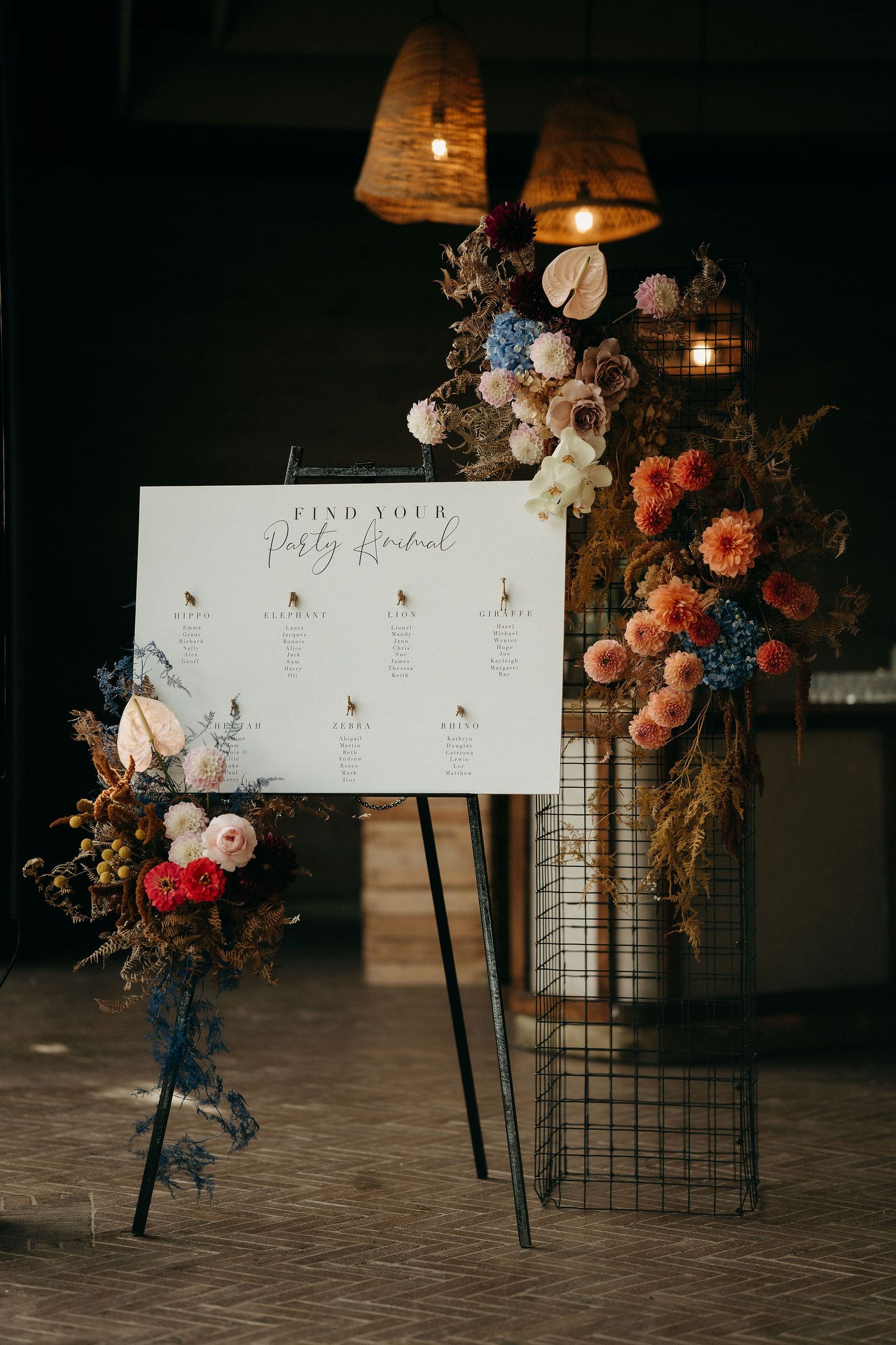 Elegant wedding seating chart display with floral arrangements and warm lighting against dark backdrop.