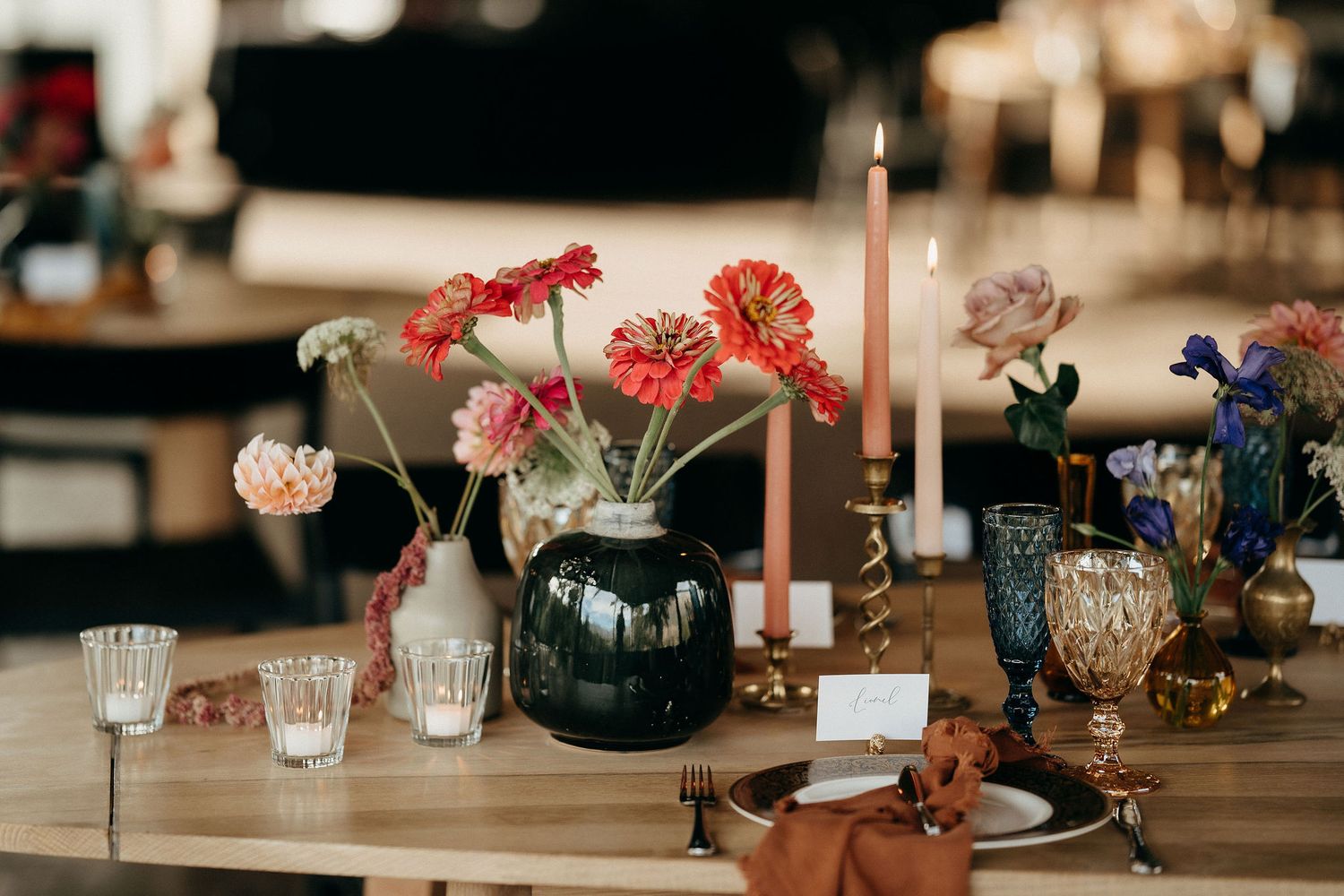 An elegant table setting with pink carnations in a navy vase, taper candles, and vintage glassware for a rustic reception.