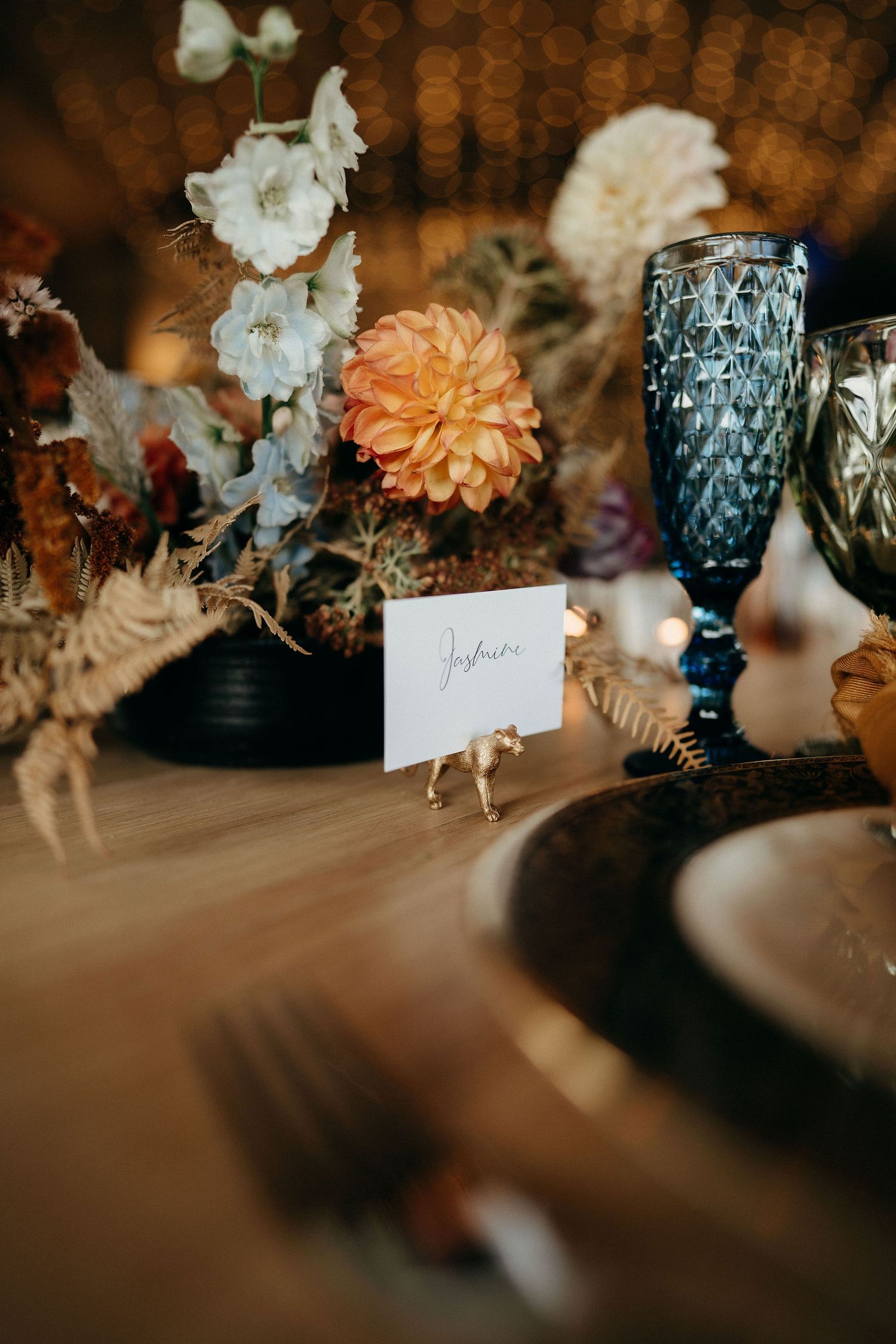 Elegant table setting with ornate blue glassware and delicate floral arrangements in warm autumn tones.