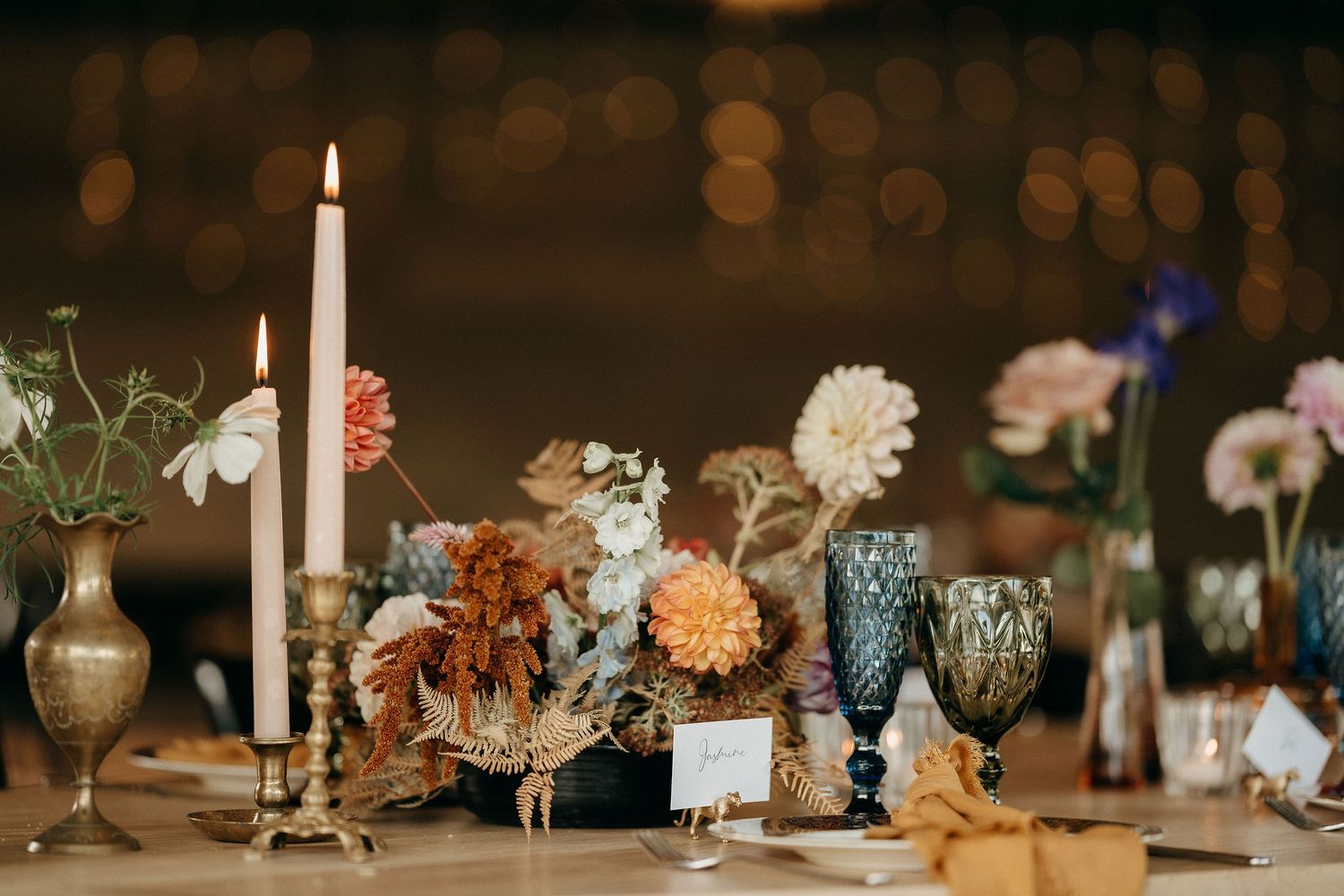 Elegant wedding table setting with lit candle, dried autumn flowers and vintage glassware on rustic wooden surface.