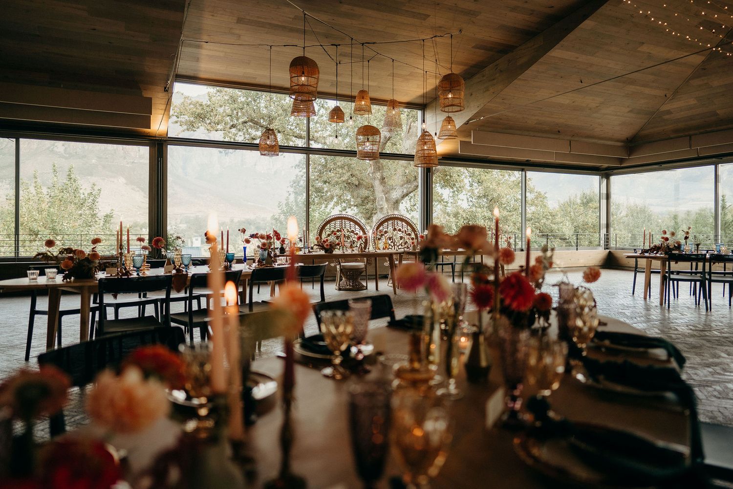 Rustic wedding reception venue with glass walls, wood ceiling, and floral centerpieces on elegant dining tables.