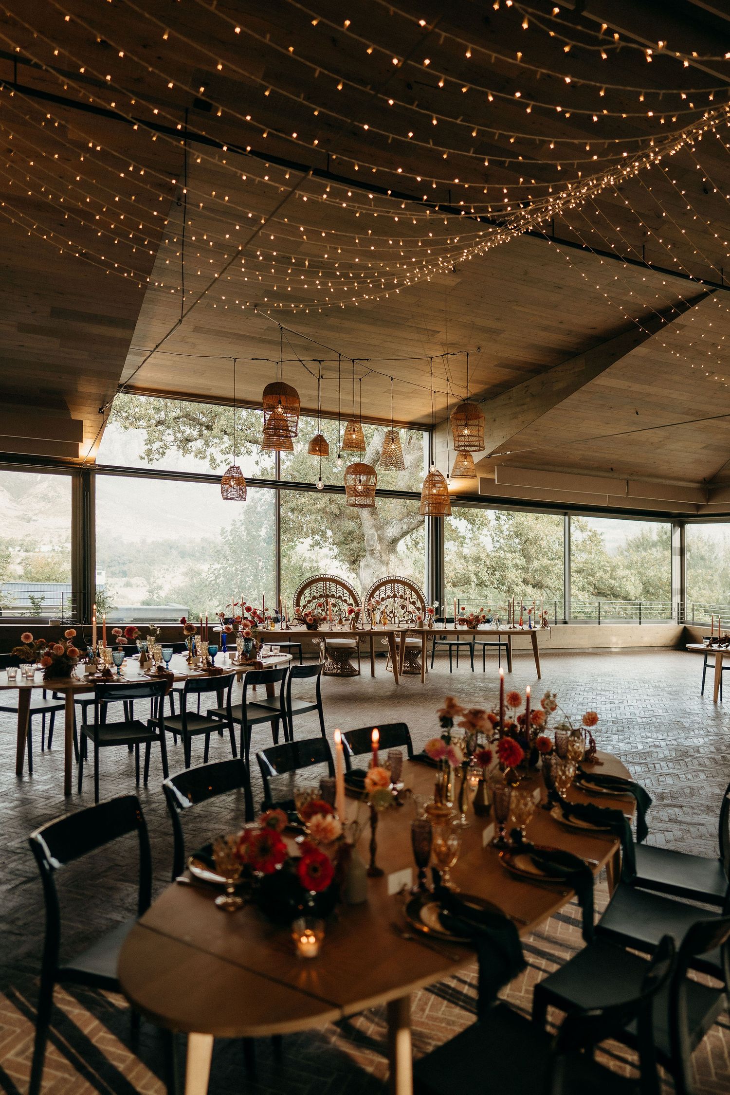 A rustic indoor venue decorated with string lights, rattan chairs, and wooden tables for a romantic wedding reception.