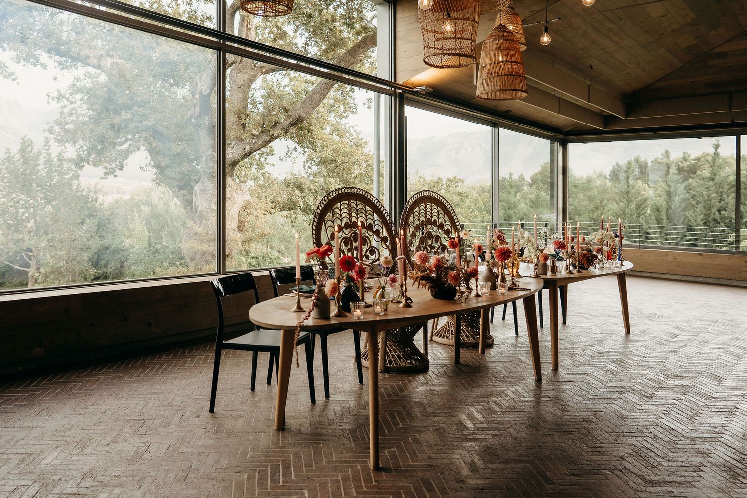 Elegant wedding reception table setup in glass-walled venue with wooden floors and forest views through large windows.