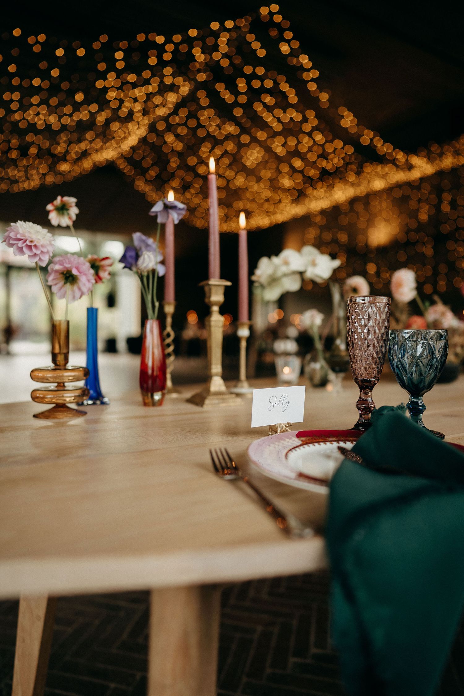 Elegant wedding table setting with vintage candlesticks, delicate flowers, and warm string lights glowing overhead.