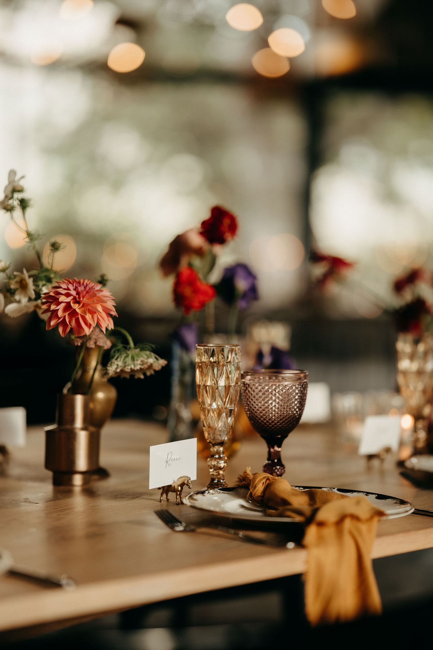 Elegant table setting with pink dahlia flowers, gold vases, crystal stemware and ambient bokeh lighting in background.