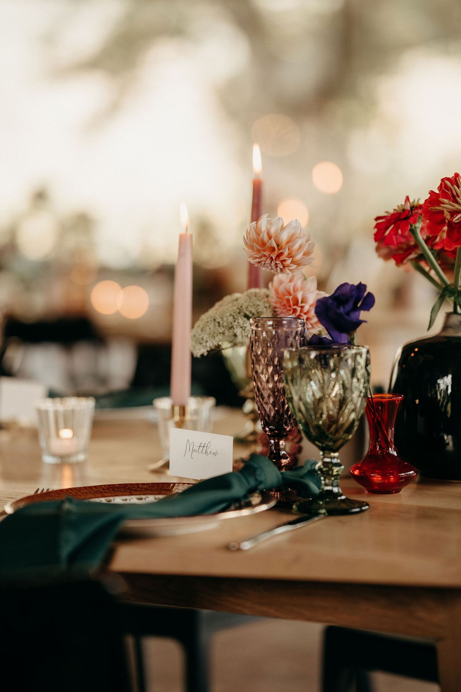 Romantic table setting with lit candles, pink and red flowers in vintage vases, and elegant place settings.