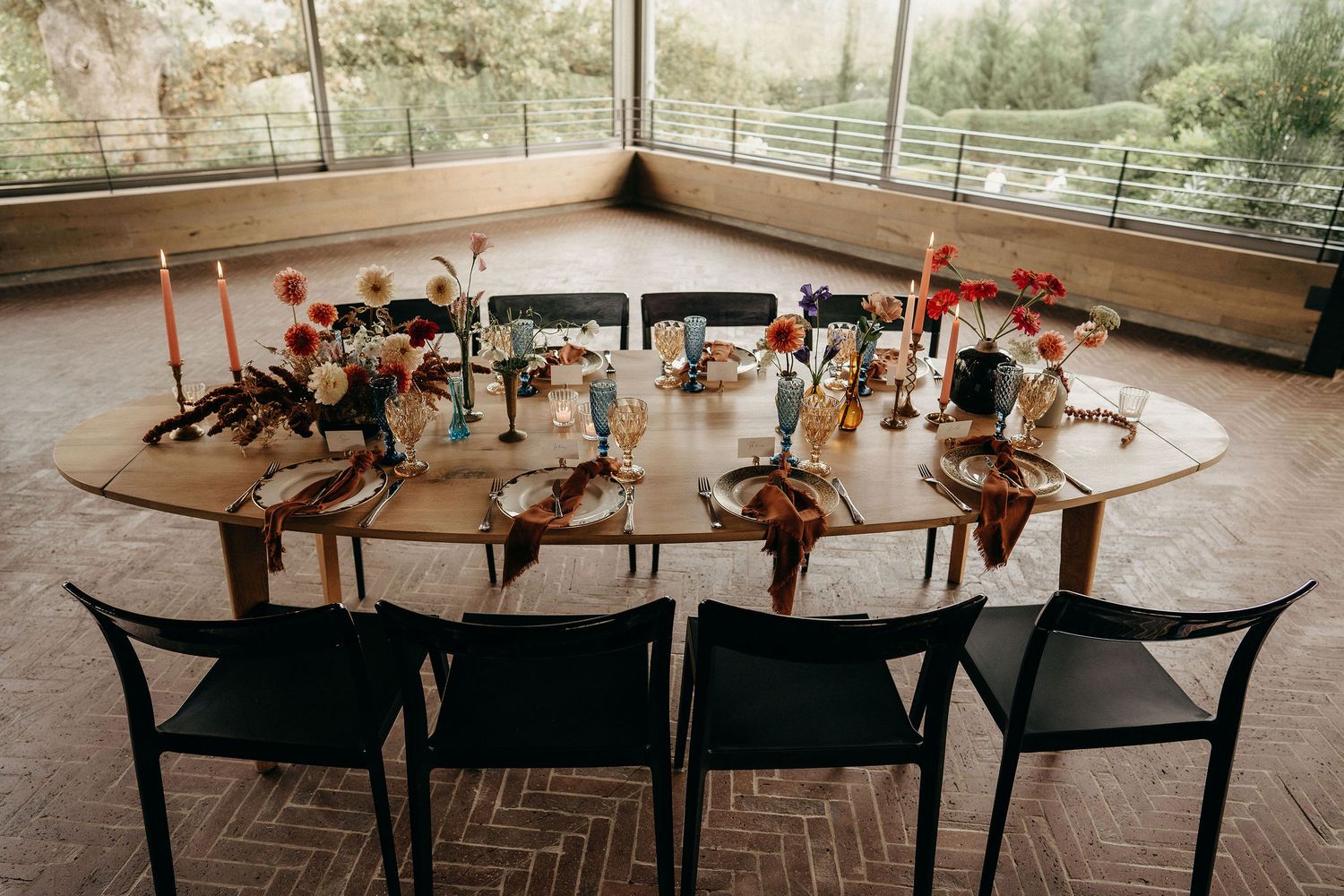 A rustic semicircle dining table decorated with candles and floral centerpieces on an outdoor covered patio.