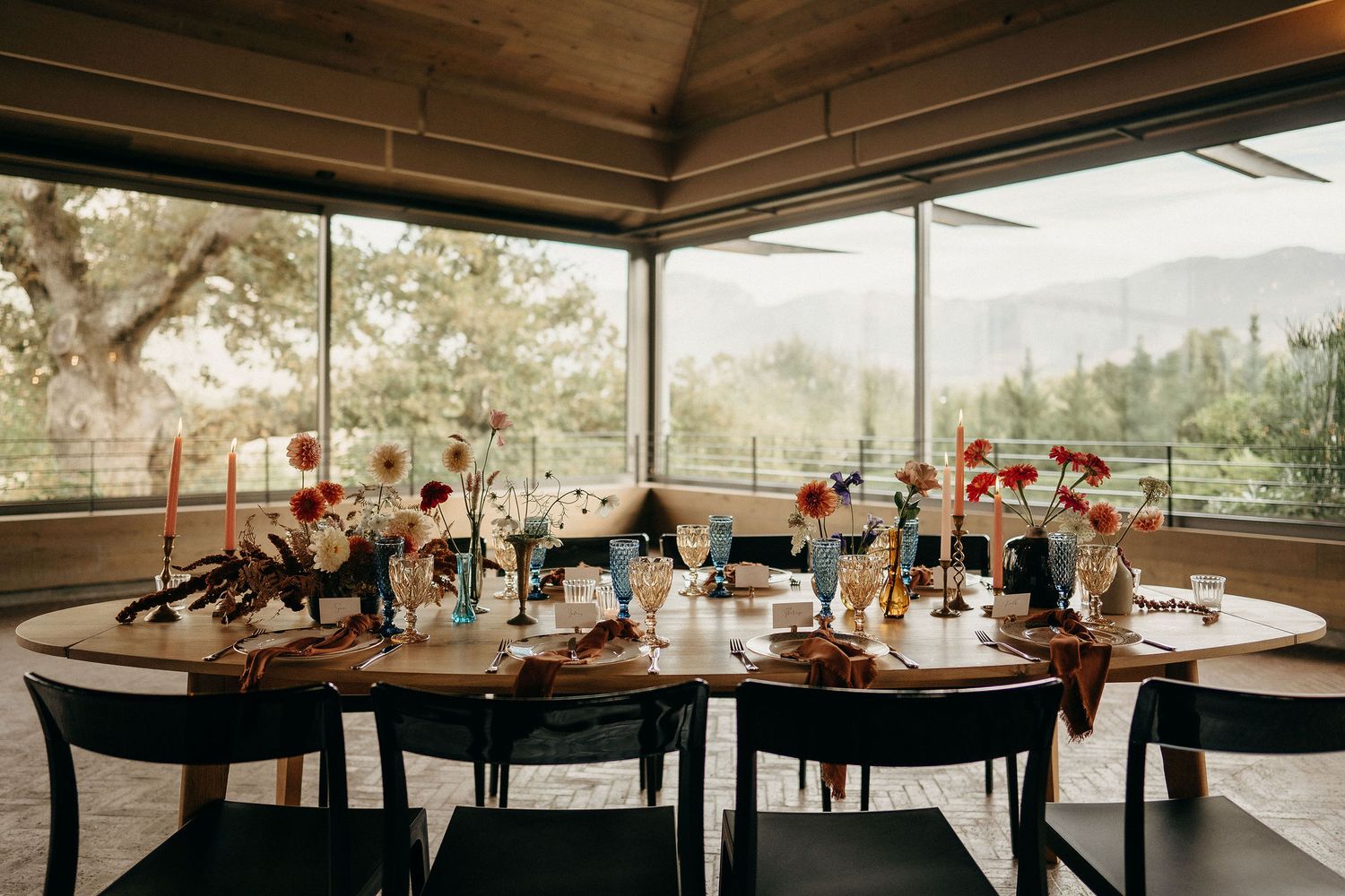 Elegant wedding table setting in a glass-enclosed venue with rustic floral centerpieces and mountain views.
