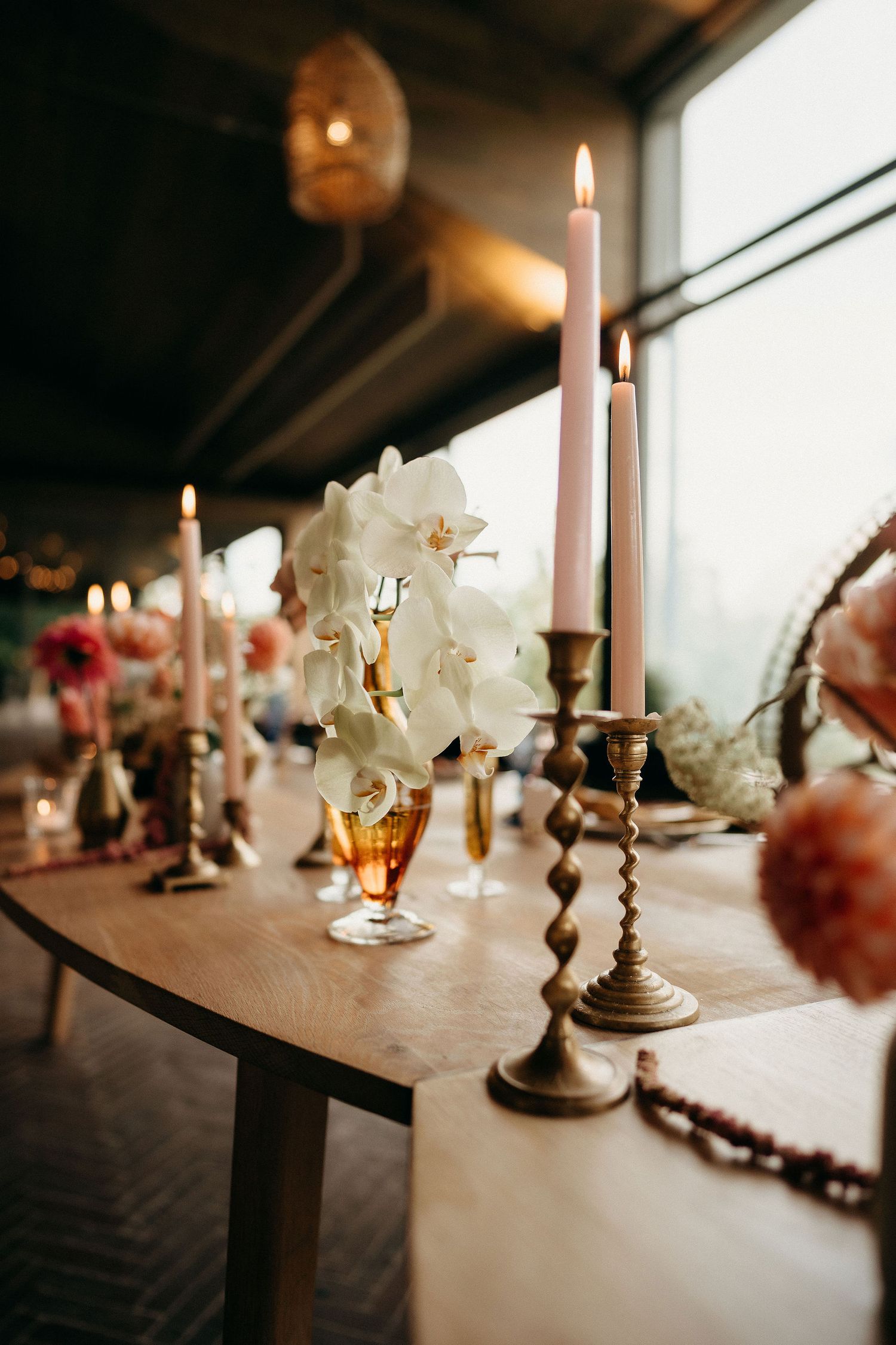 Elegant table setting with white orchids, lit candles in brass holders, and a amber glass creating a warm romantic ambiance.