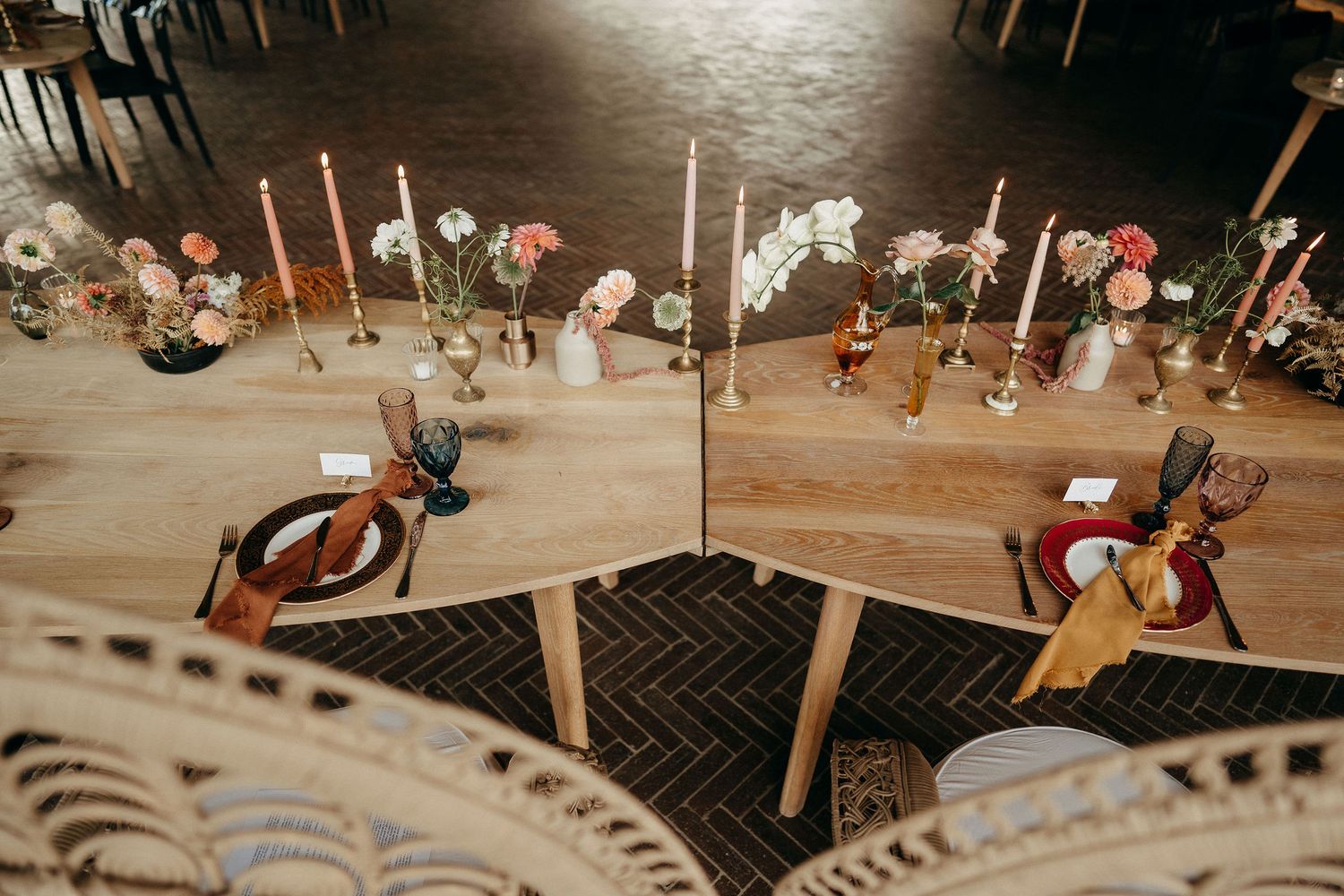 Looking down at a rustic wedding reception table decorated with pink flowers, candles and tableware on a wooden floor.