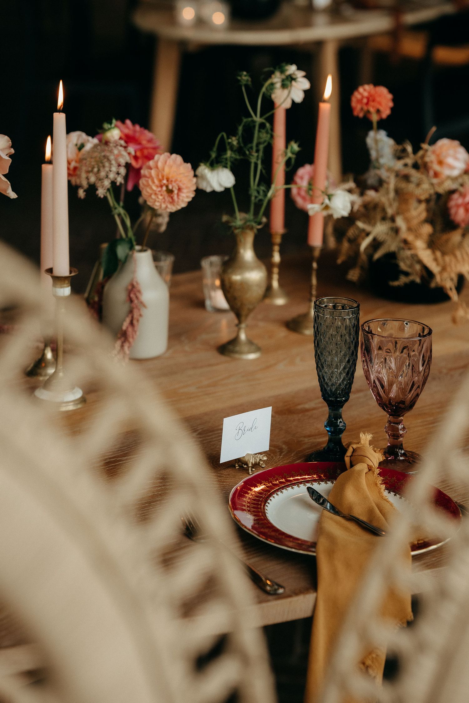 Elegant table setting with vintage glassware, lit candles, pink carnations and place cards on a wooden surface.