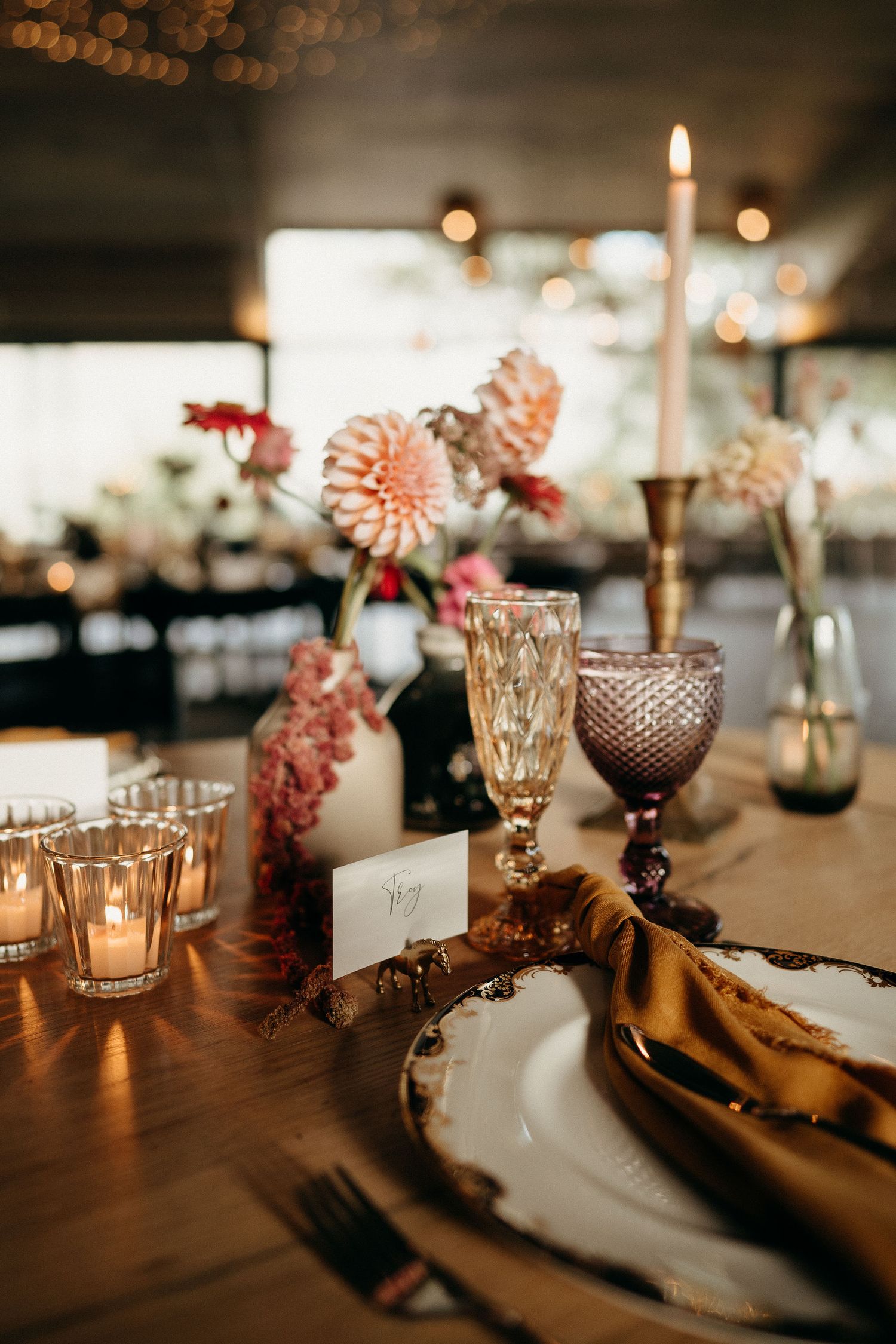 Elegant table setting with pink flowers, vintage glassware, gold candles and romantic mood lighting for an upscale event.
