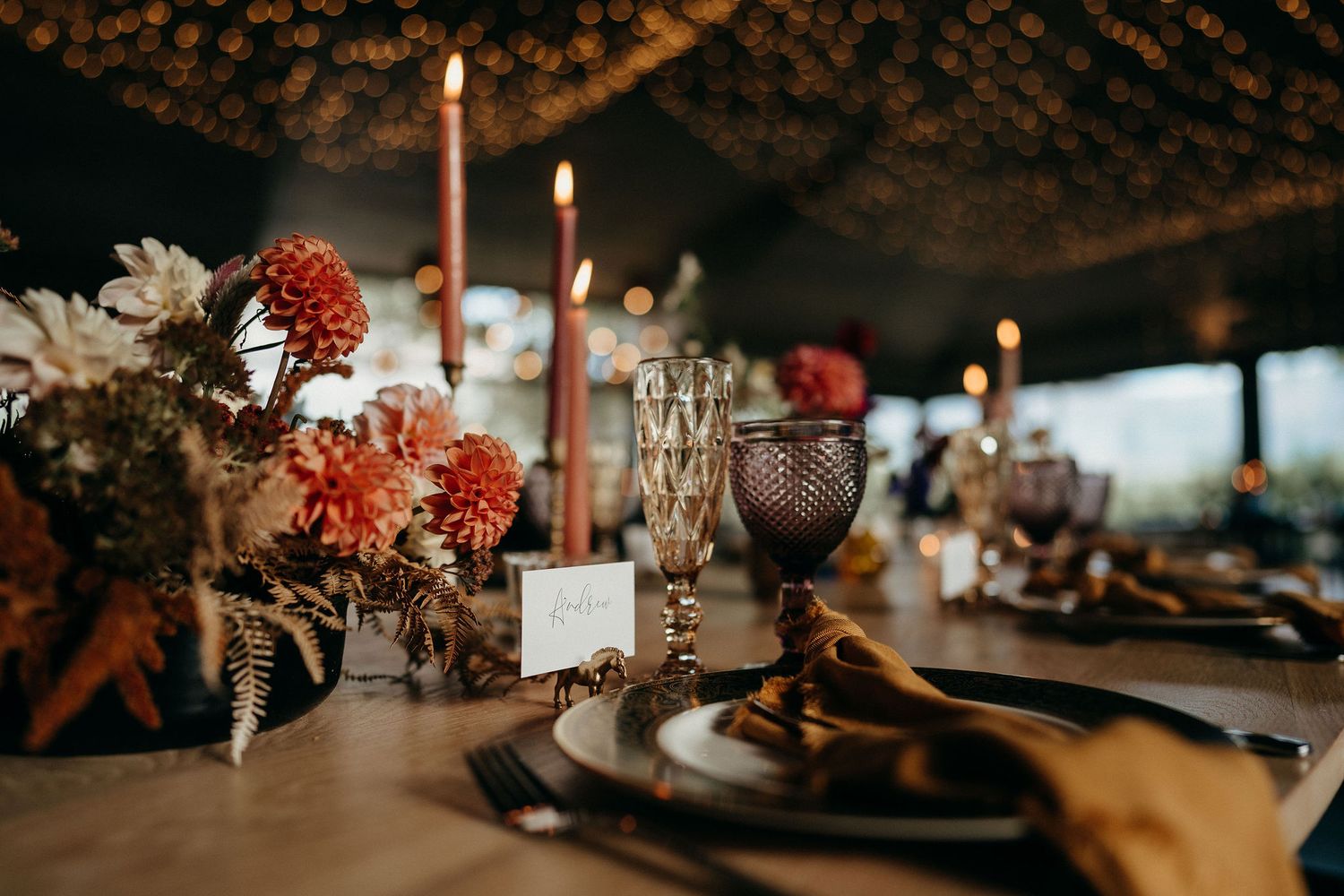 Elegant wedding reception table setting with moody lighting, tall candles, and autumn-colored floral arrangements.