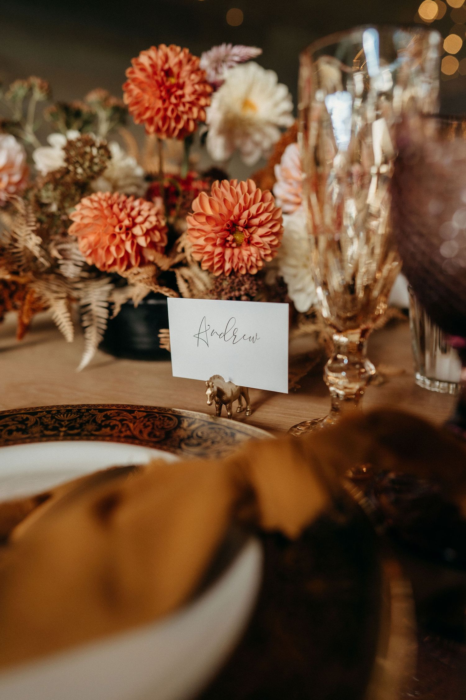 Elegant table setting with coral dahlias, dried flowers, and a place card holder featuring a small golden elephant detail.