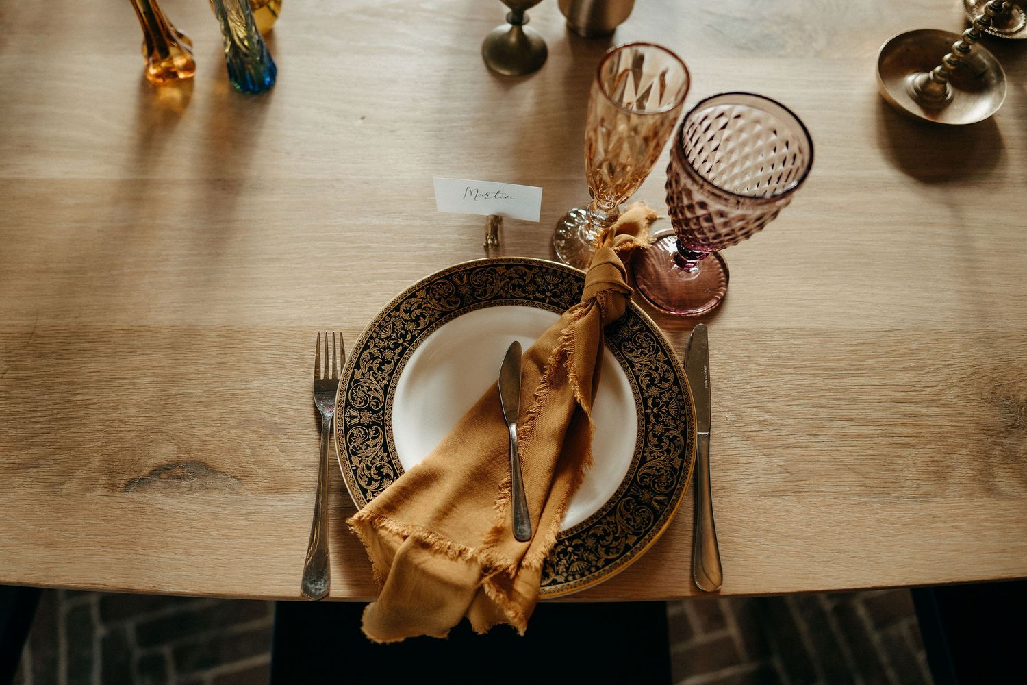 Elegant table setting with ornate plate, crystal wine glass and gold napkin artfully arranged on wooden surface.