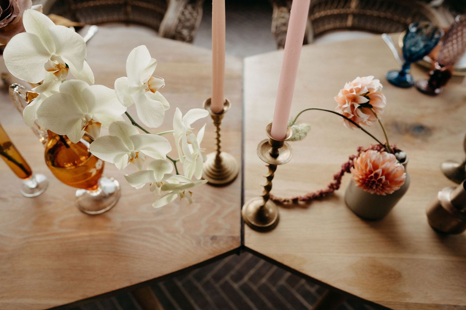 White orchids and pink carnations in vases with brass candlesticks on wooden table create an elegant centerpiece display.