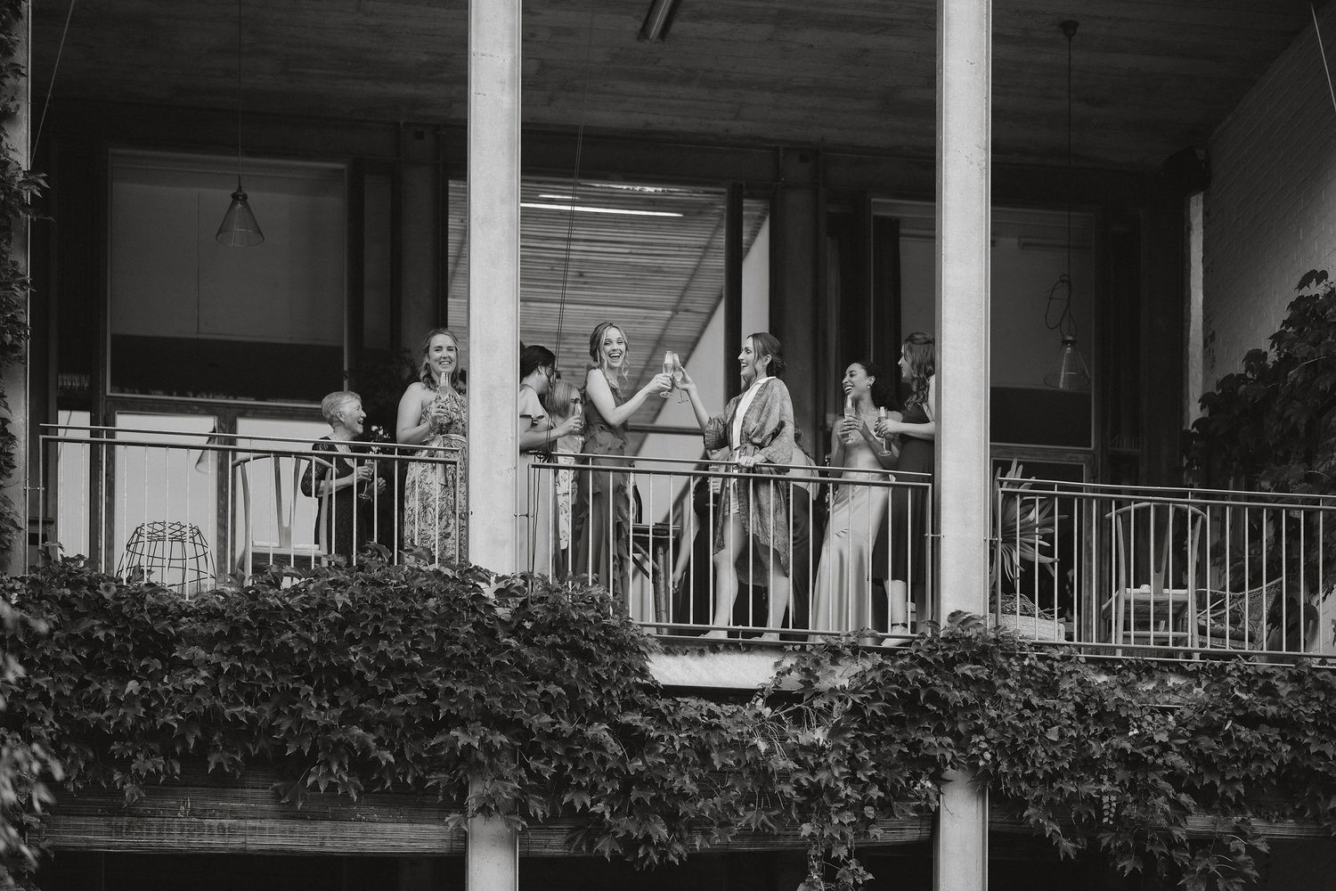 People gather on a vintage porch railing with ivy growing beneath in this black and white photograph.
