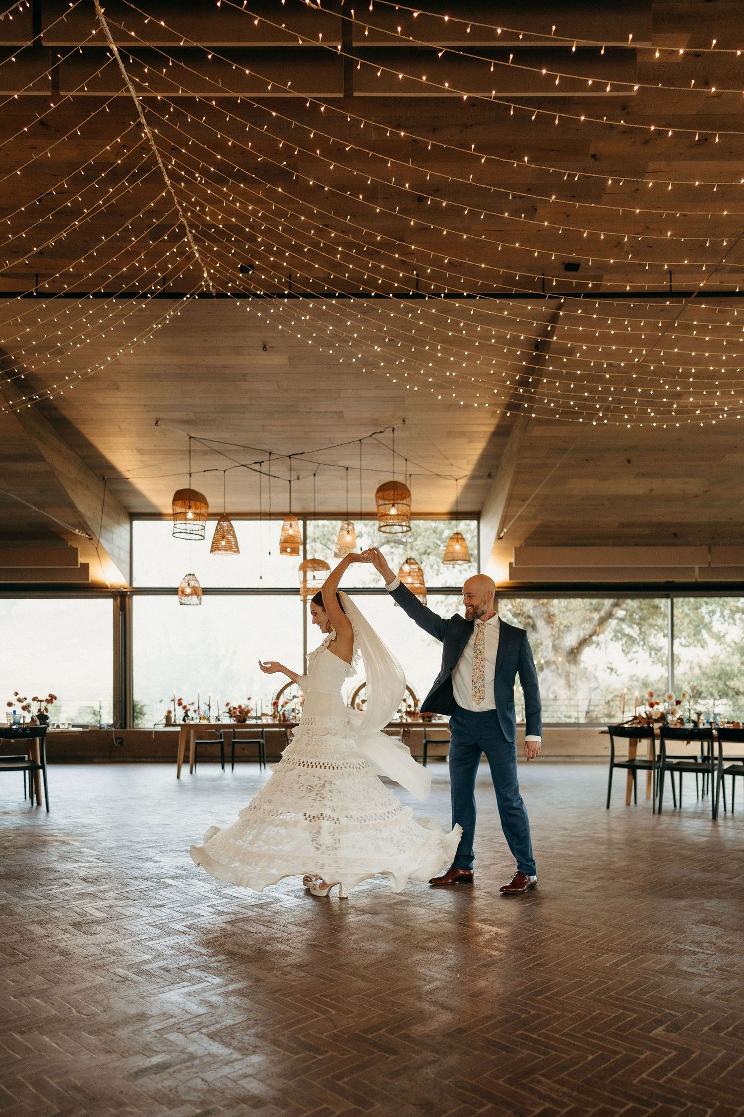 A couple dancing in a wedding reception venue with twinkle lights strung across the ceiling and wooden parquet flooring.
