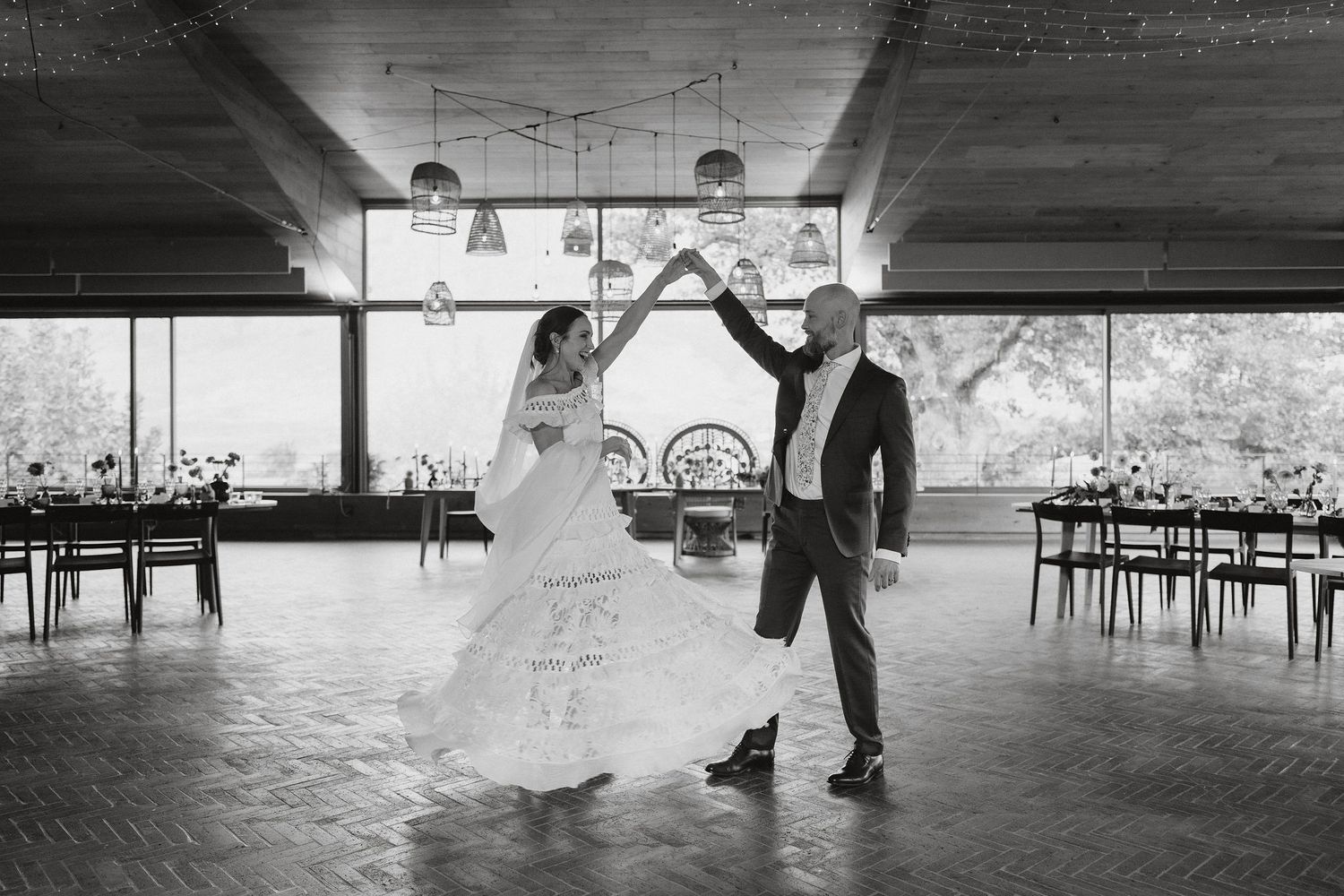 A black and white photo shows a couple dancing together on a wooden floor in an elegant venue.